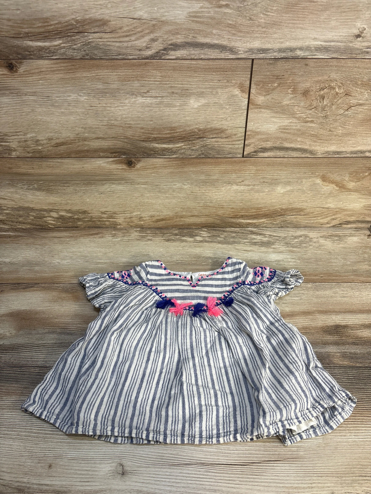 Striped baby dress with pink and navy tassel accents on wood background, gently used