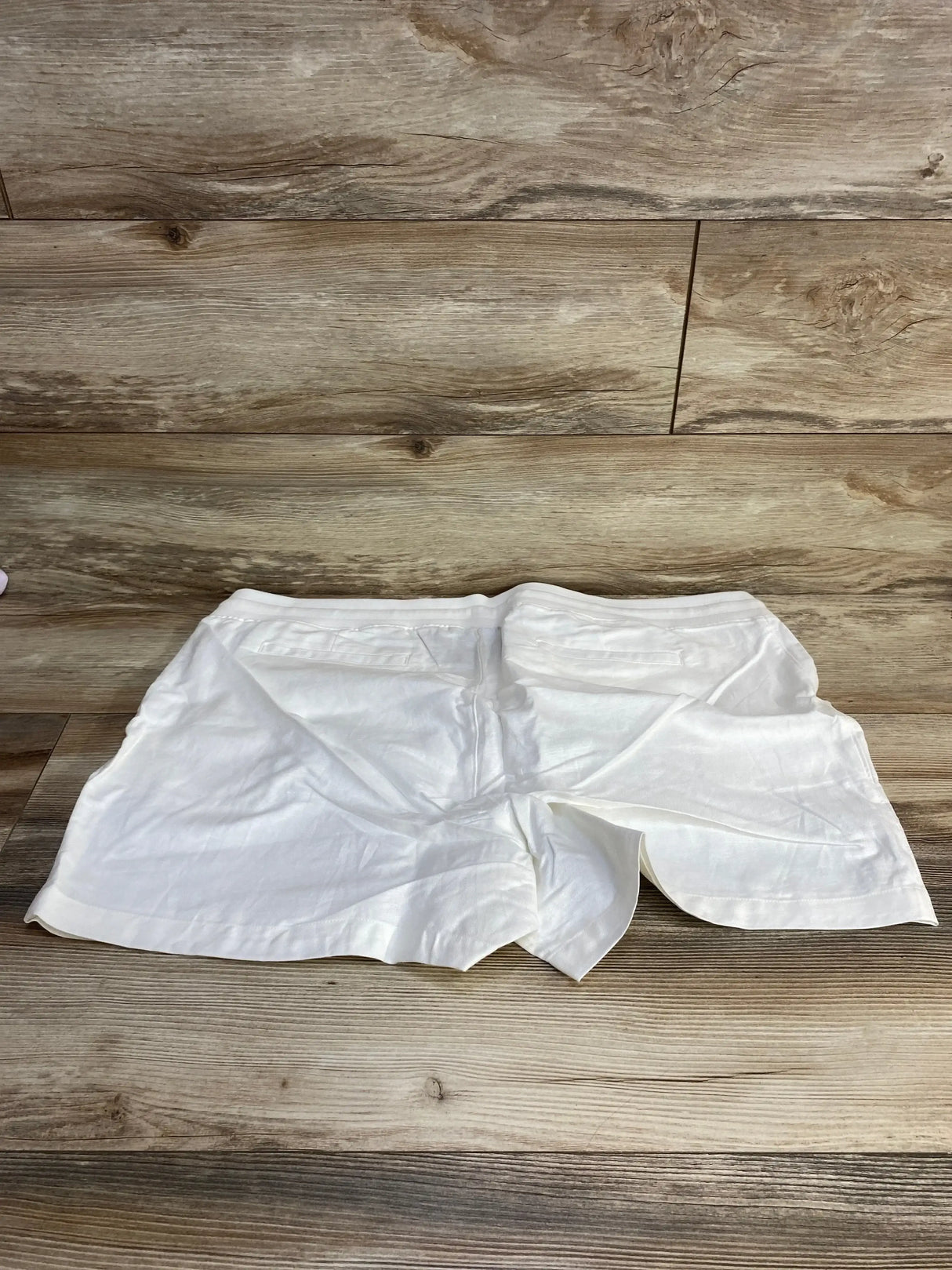Flat-lay back view of white maternity linen shorts size XXL with elastic waistband and back welt pockets on wood floor