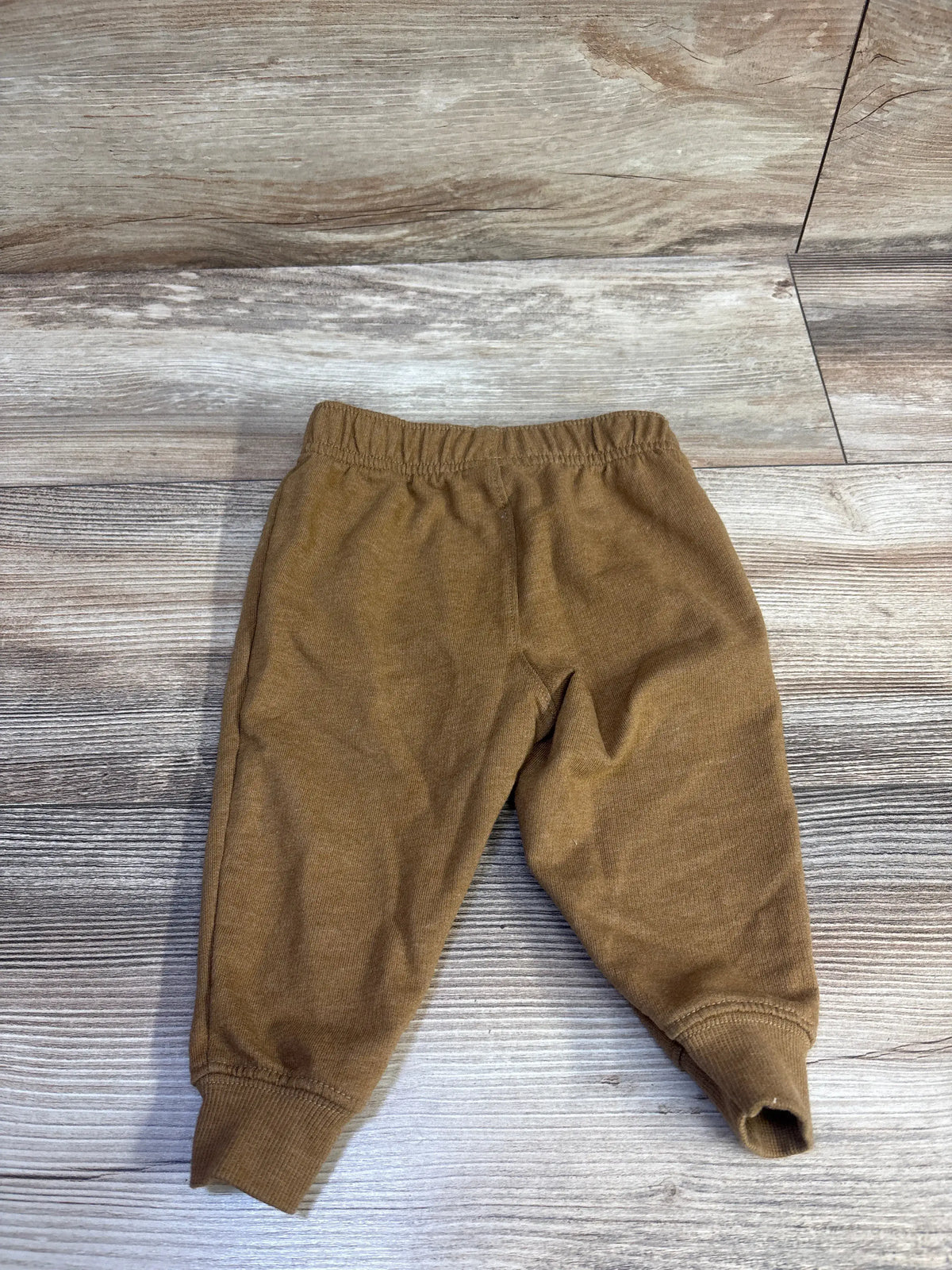 Brown Carter's pull-on joggers for infants size 12m on a light wood background