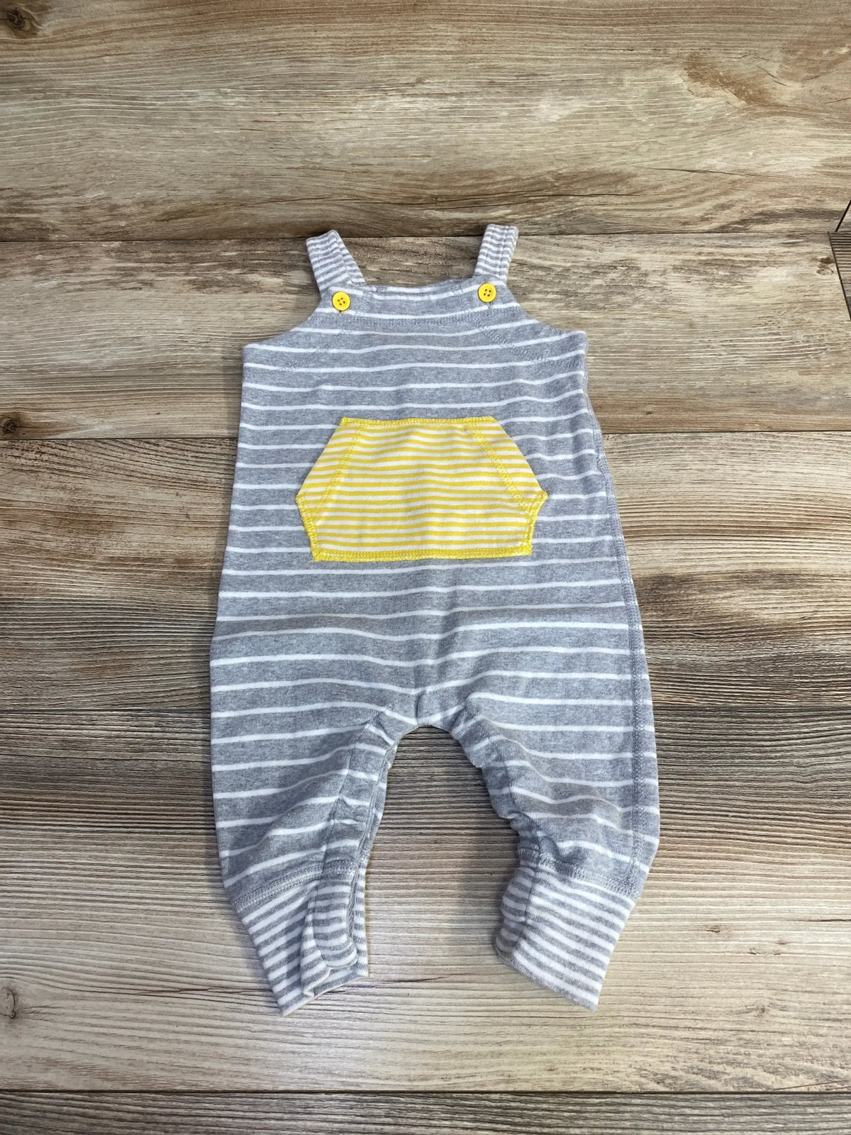 Front view of grey and white striped organic baby shortall with yellow pocket and yellow button straps on wood background