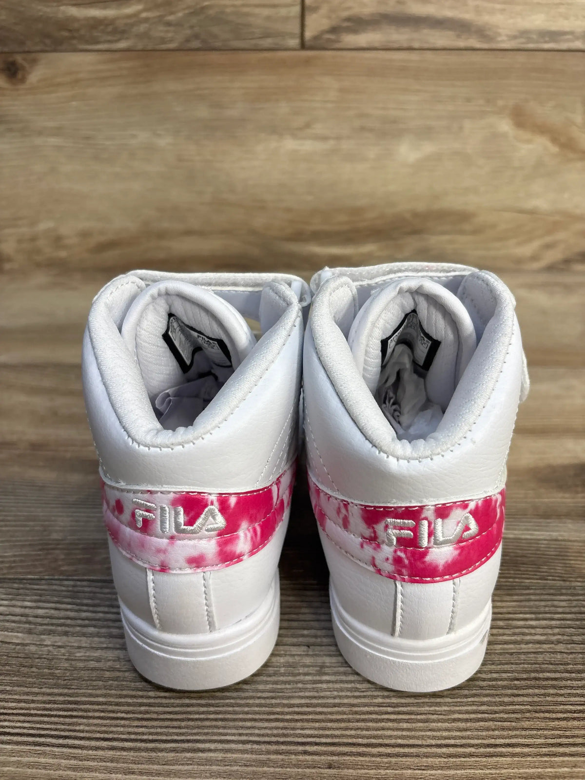 White FILA kids sneakers with pink tie-dye detail on wooden floor