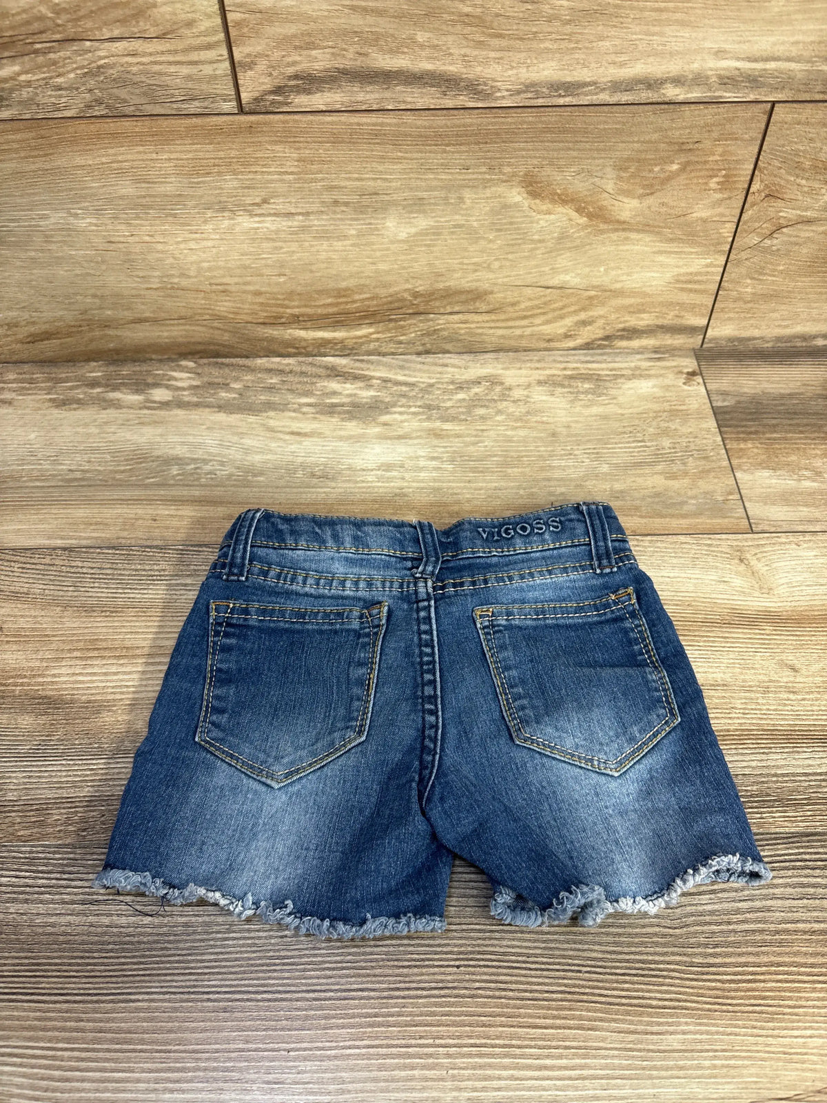 Back view of Vigoss The Malibu mid-shorts showcasing two back pockets and frayed hems on a wood floor