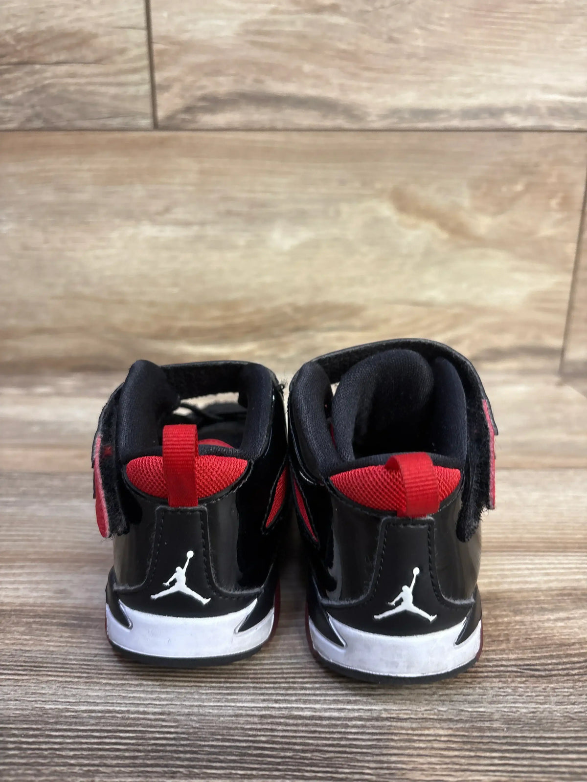 Back view of Jordan Flight Club 91 ‘Bred’ toddler sneakers showing black patent, red accents and Jumpman logo on wood floor