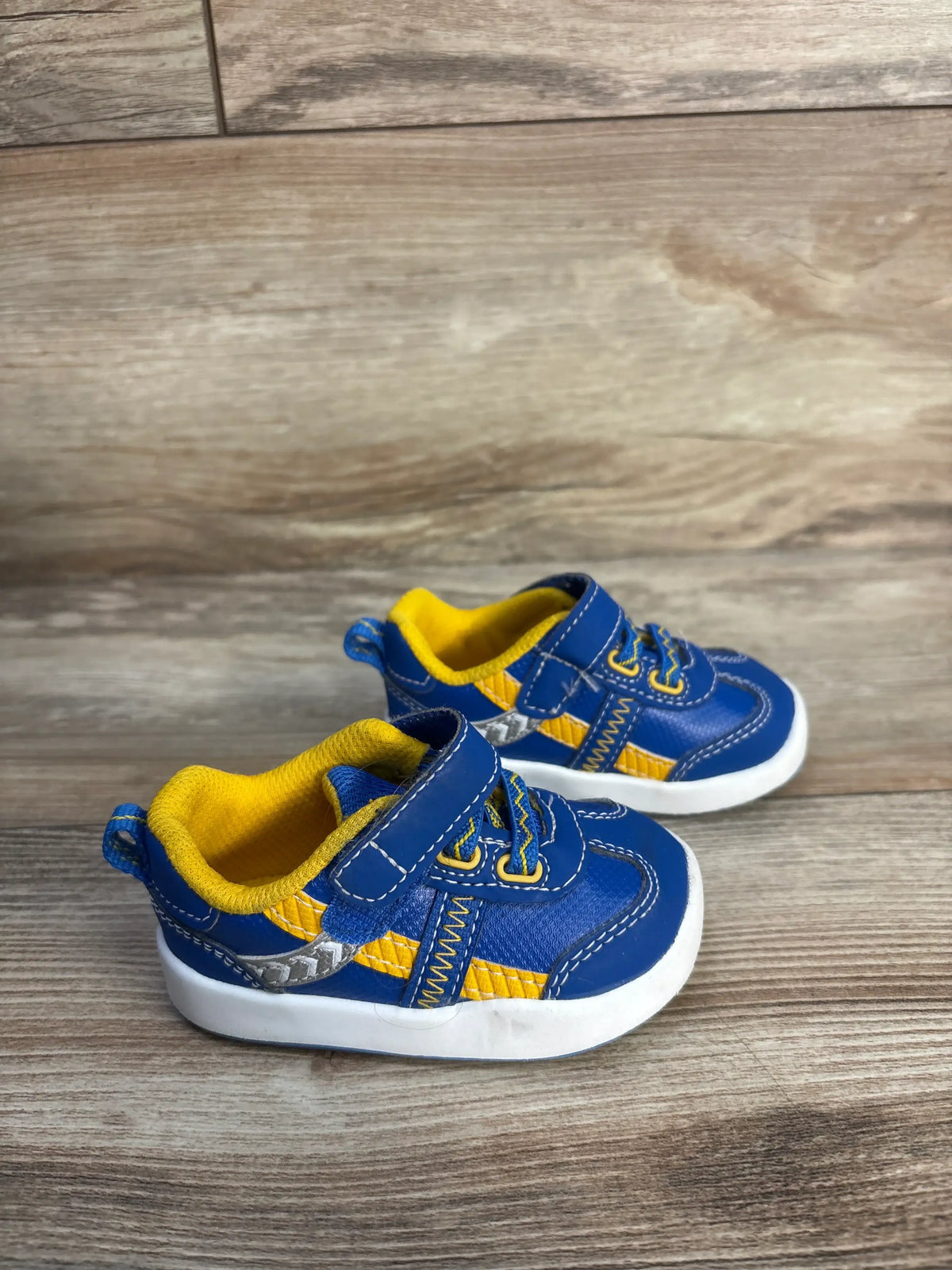 Side view of Wonder Nation blue sneakers, size 3C, with yellow accents, Velcro straps, and cushioned soles on a wood floor