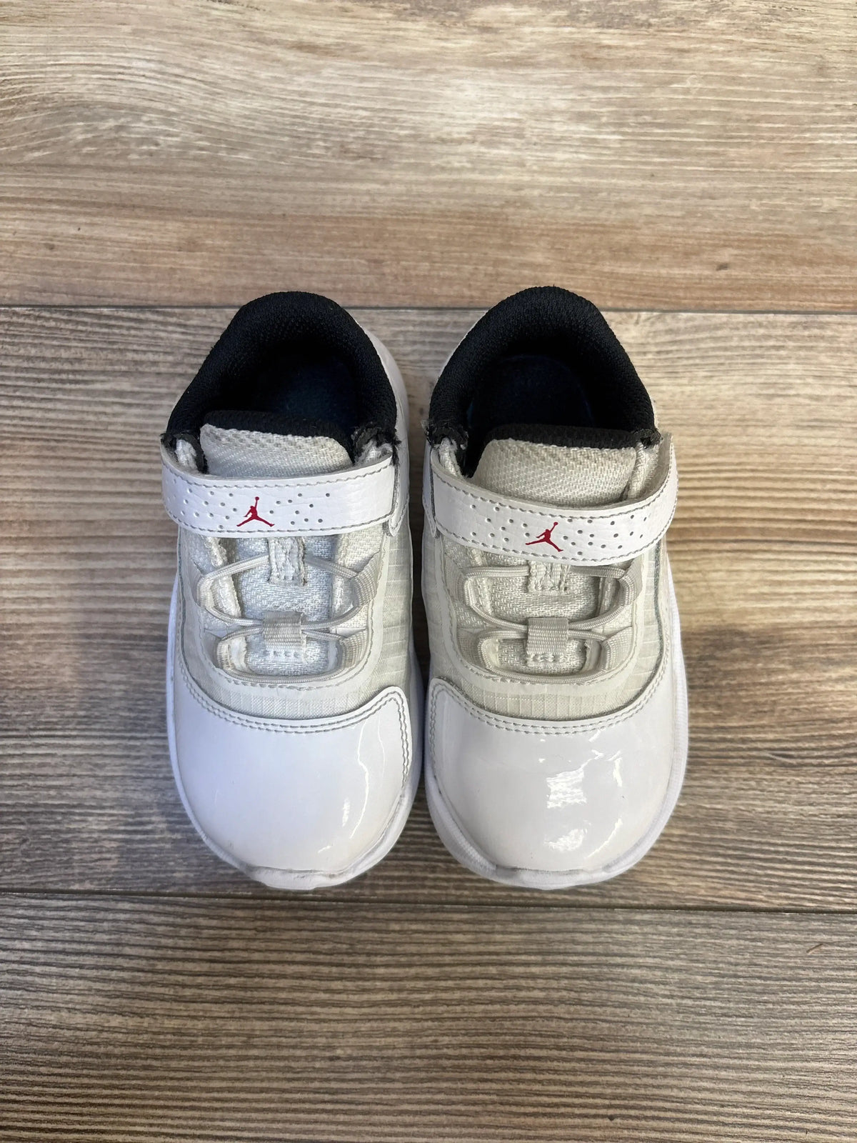 Top view of Air Jordan 11 CMFT Low GS toddler sneakers, white with red Jumpman on velcro and black collar on wood floor
