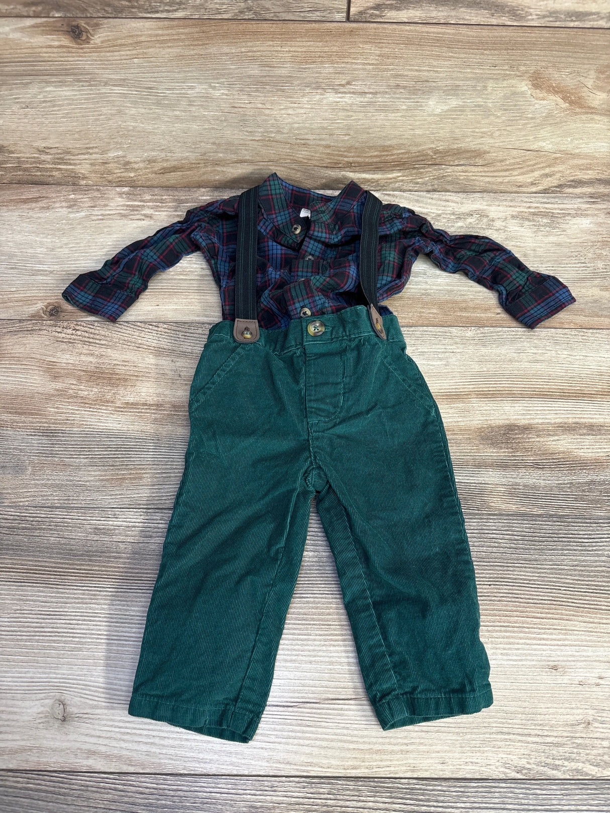 Kids green corduroy pants with suspenders and plaid shirt on wood background