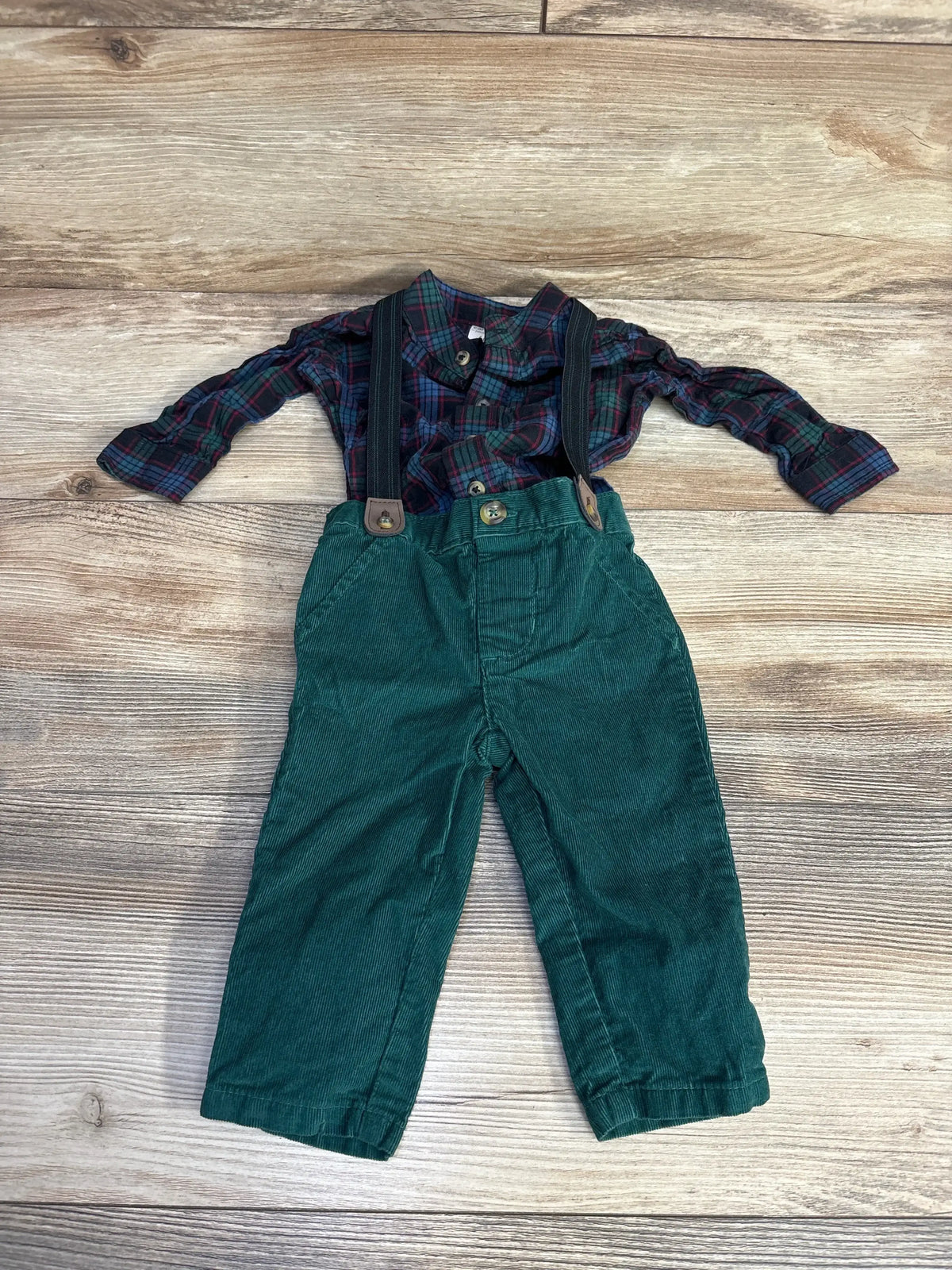 Kids green corduroy pants with suspenders and plaid shirt on wood background