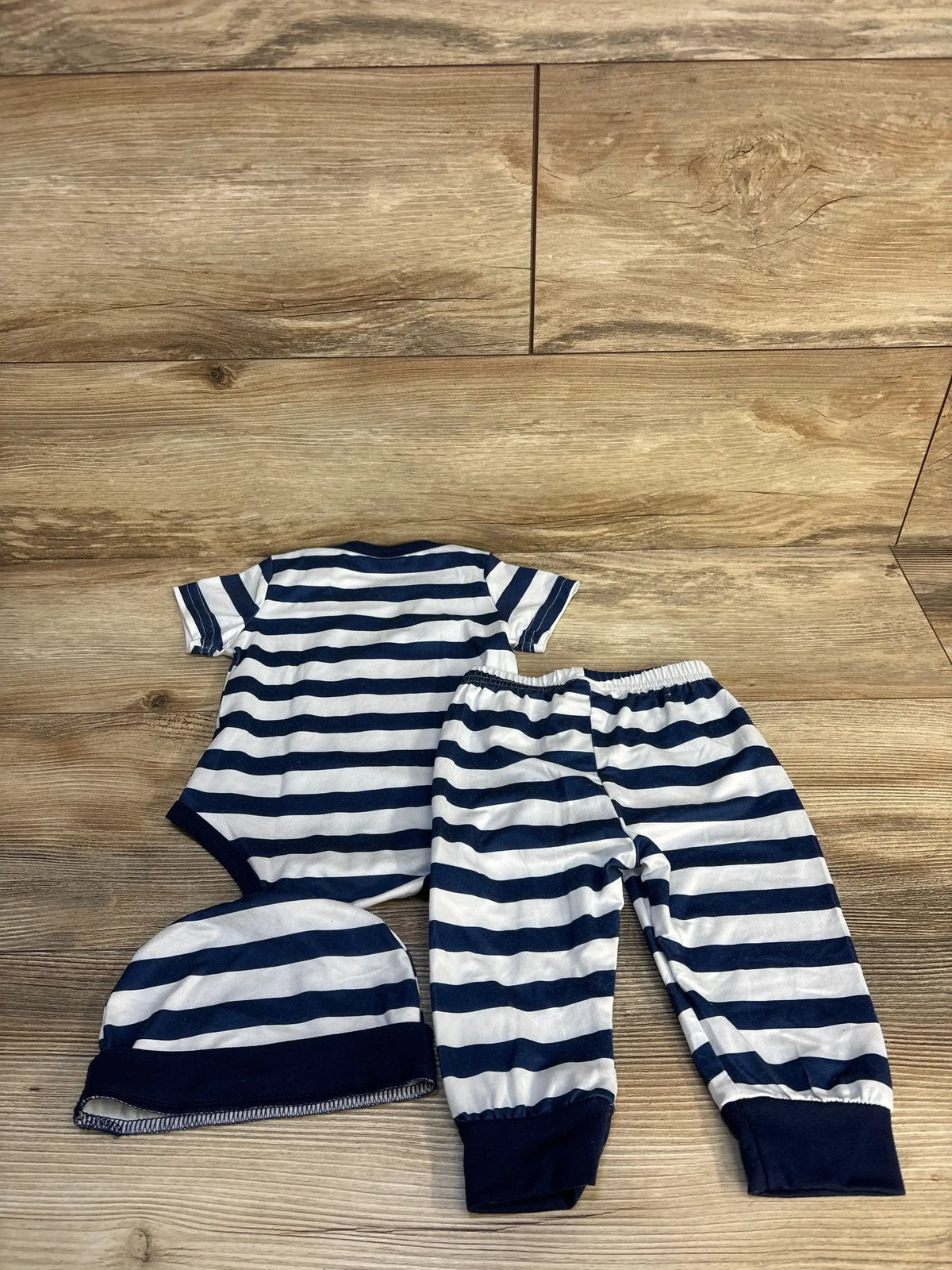 Navy and white striped baby bodysuit, pants, and hat set on wood background