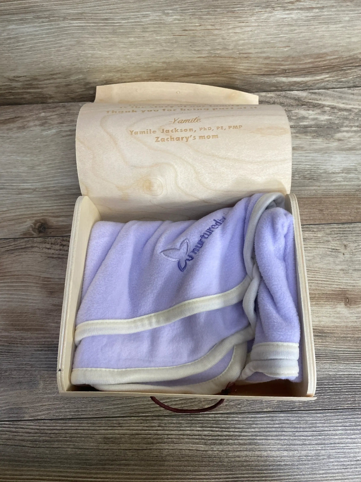 Lilac fleece baby blanket with white trim in a wooden keepsake box on wood background