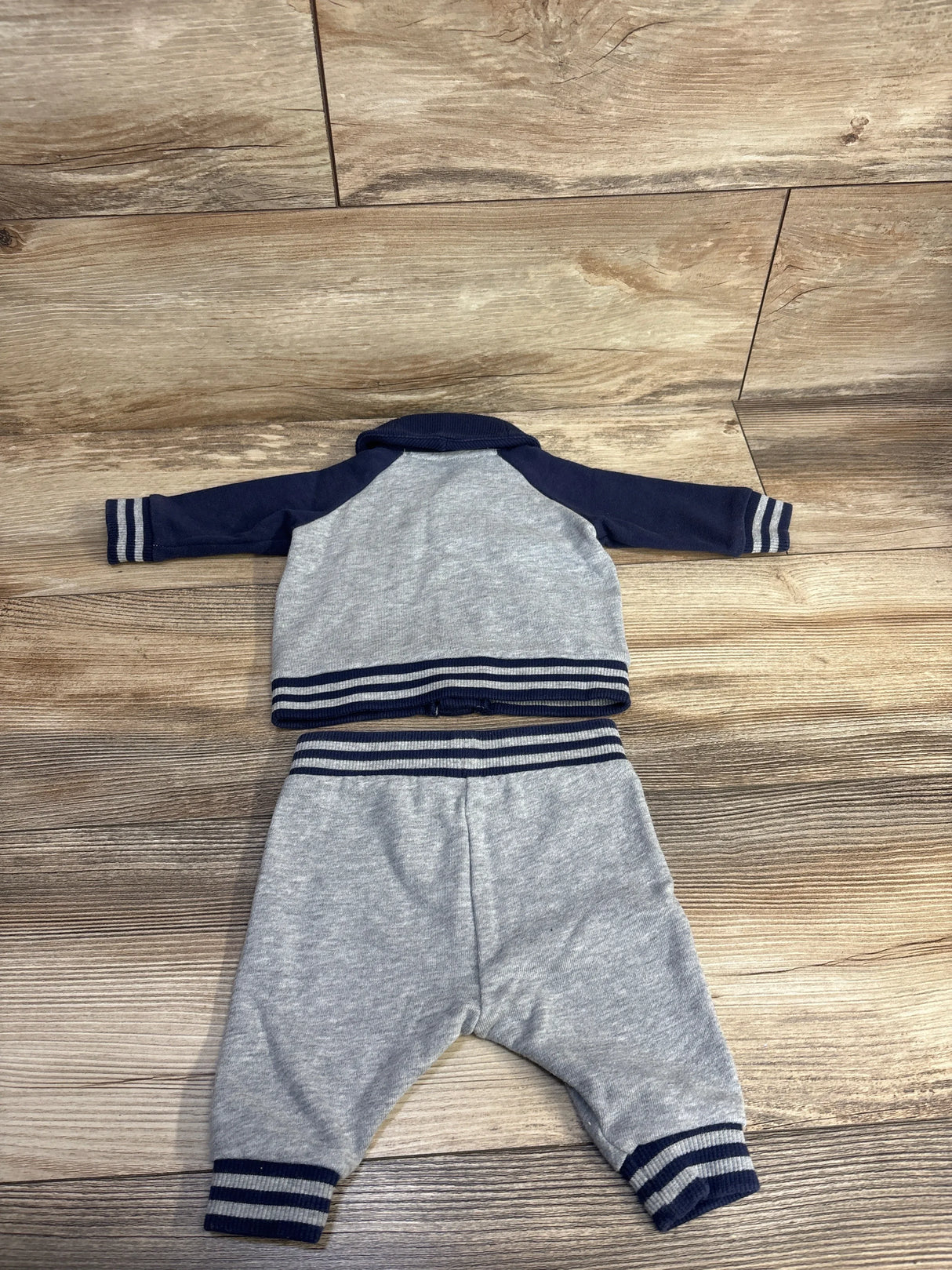 Gray baby tracksuit set with navy sleeves and striped trim on wooden background