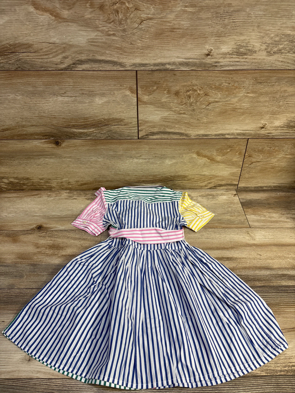 Flat-lay of Polo Ralph Lauren shirtdress size 4T with navy-white stripes, pink sash and multicolor sleeves on wood background