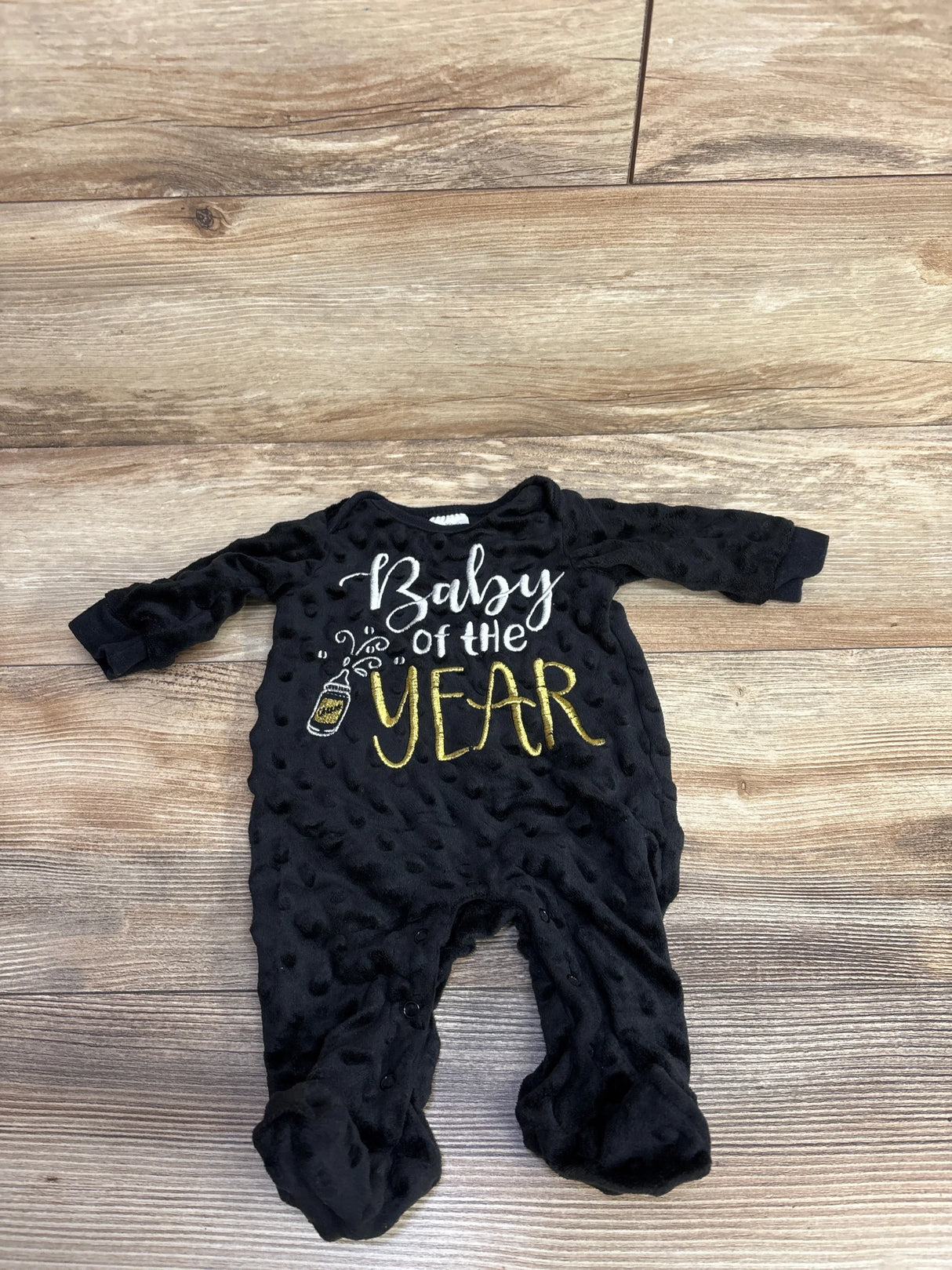 Black baby romper with 'Baby of the Year' gold and white text on wood floor