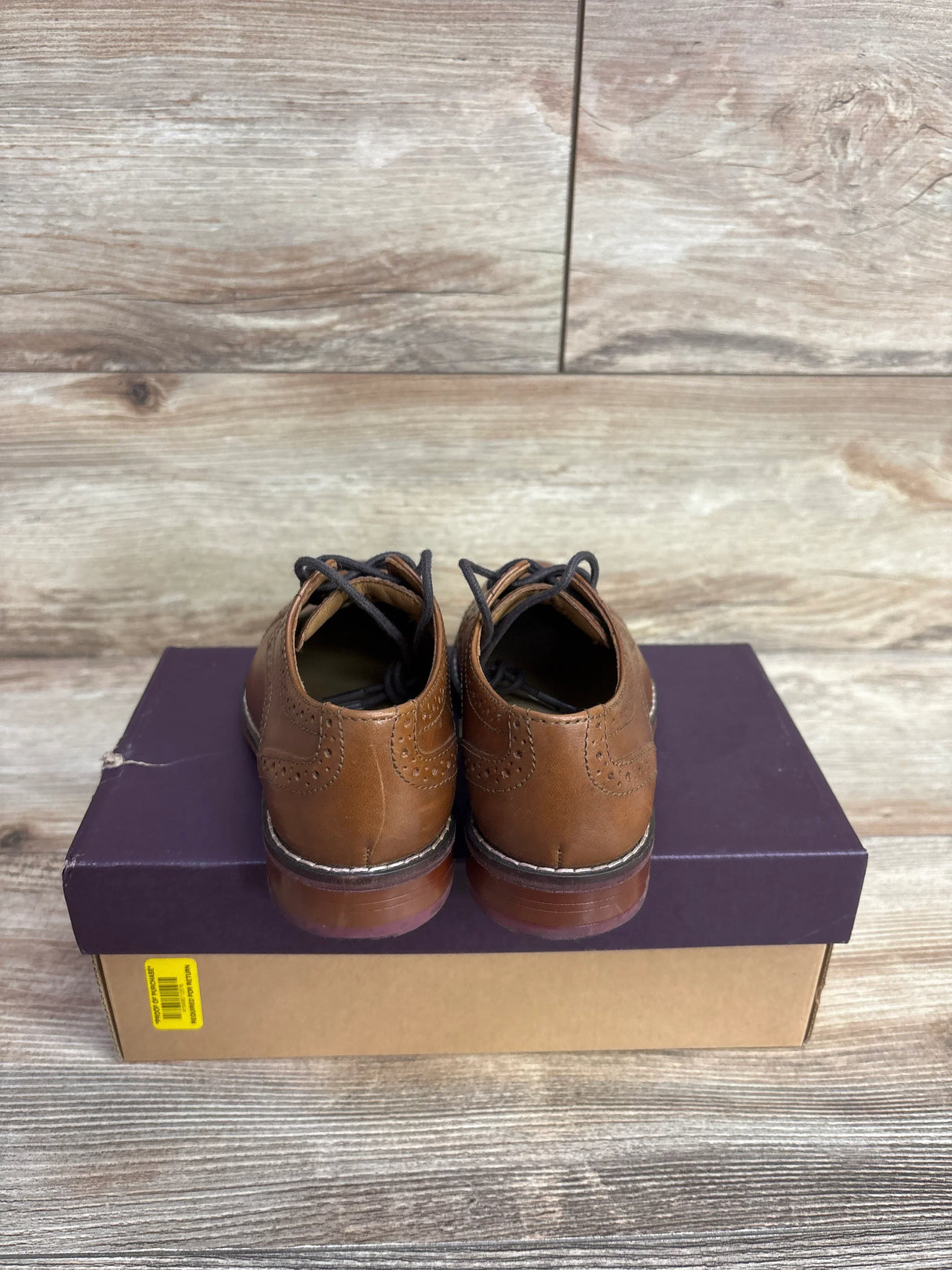 Brown leather dress shoes with black laces on purple and brown shoebox on wooden floor