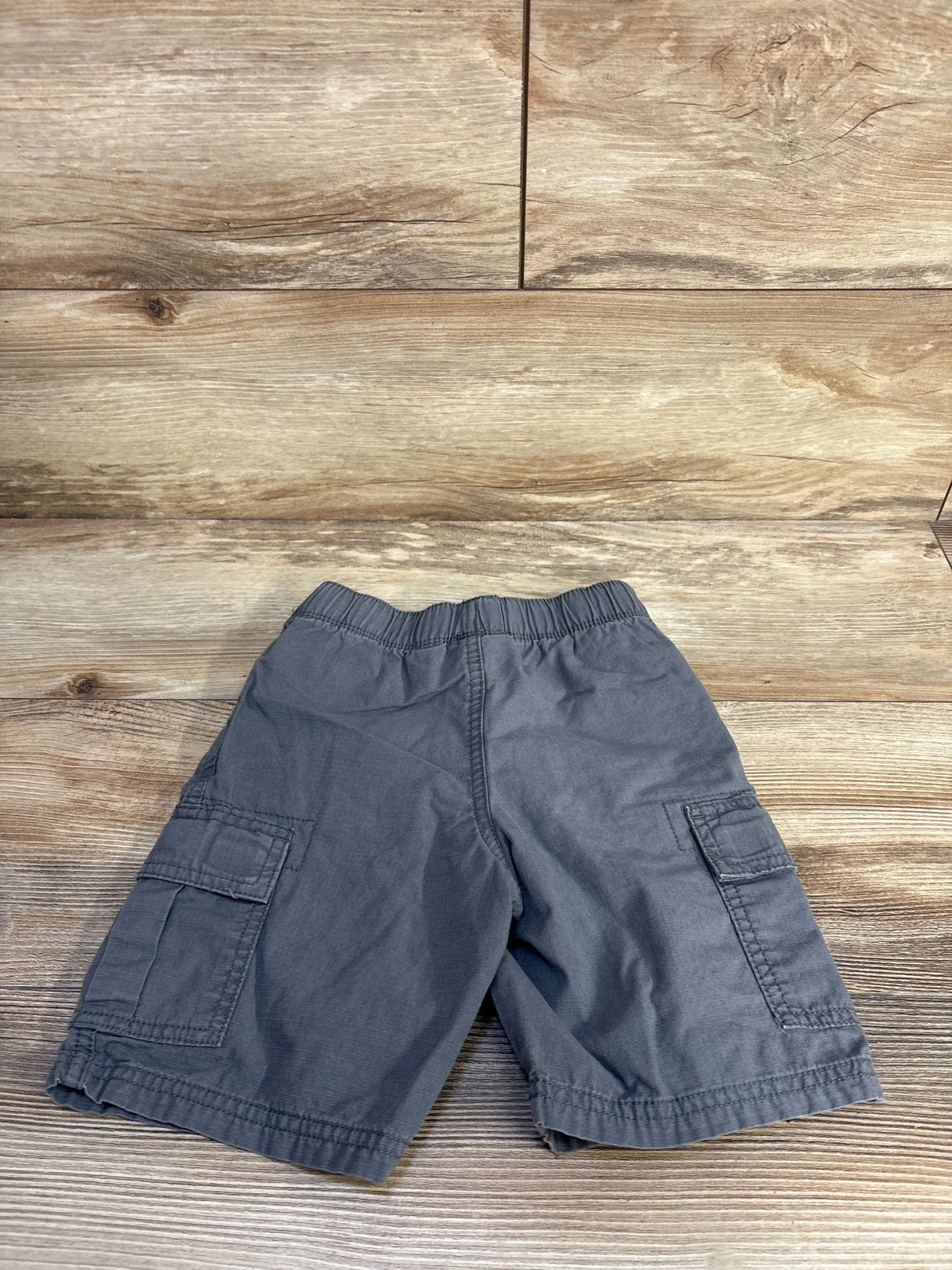 Flat lay of grey toddler cargo shorts with elastic waistband and flap side pockets on wood background