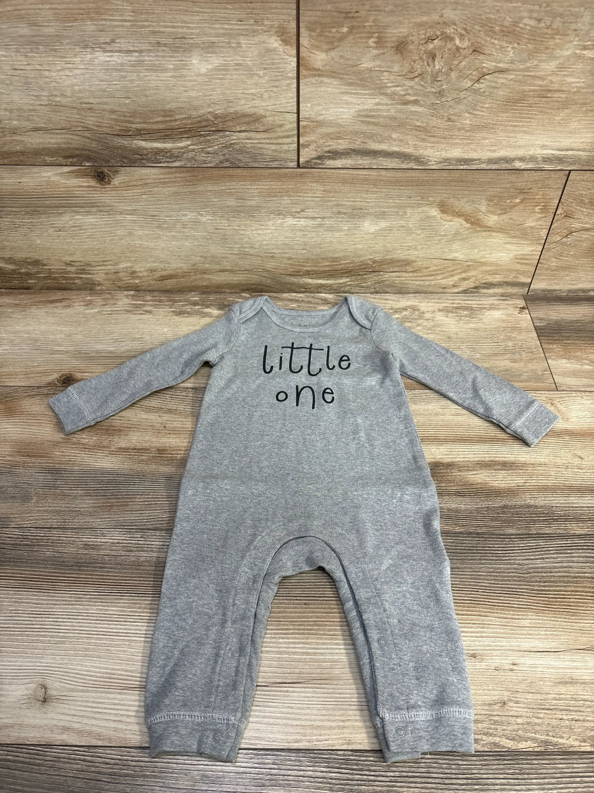 Front view of grey Little Navy Little One coverall, size 6-9 months, with long sleeves and snap closures on wood flooring