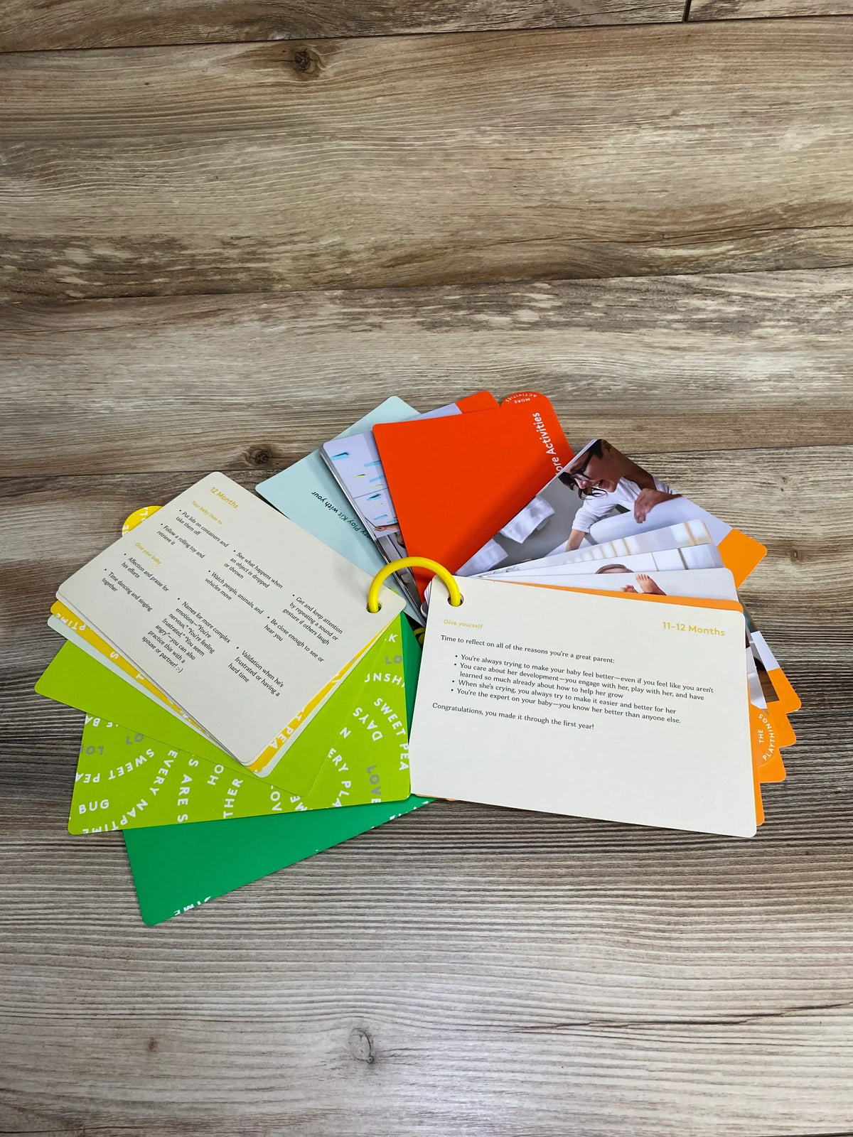Top-down view of Lovevery The Thinker Play Guide ring-bound flashcards fanned open showing ‘11-12 Months’ on wood