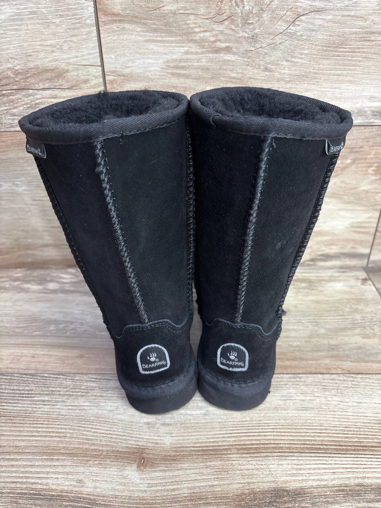 Pair of black Bearpaw kids winter boots with plush lining on wooden floor