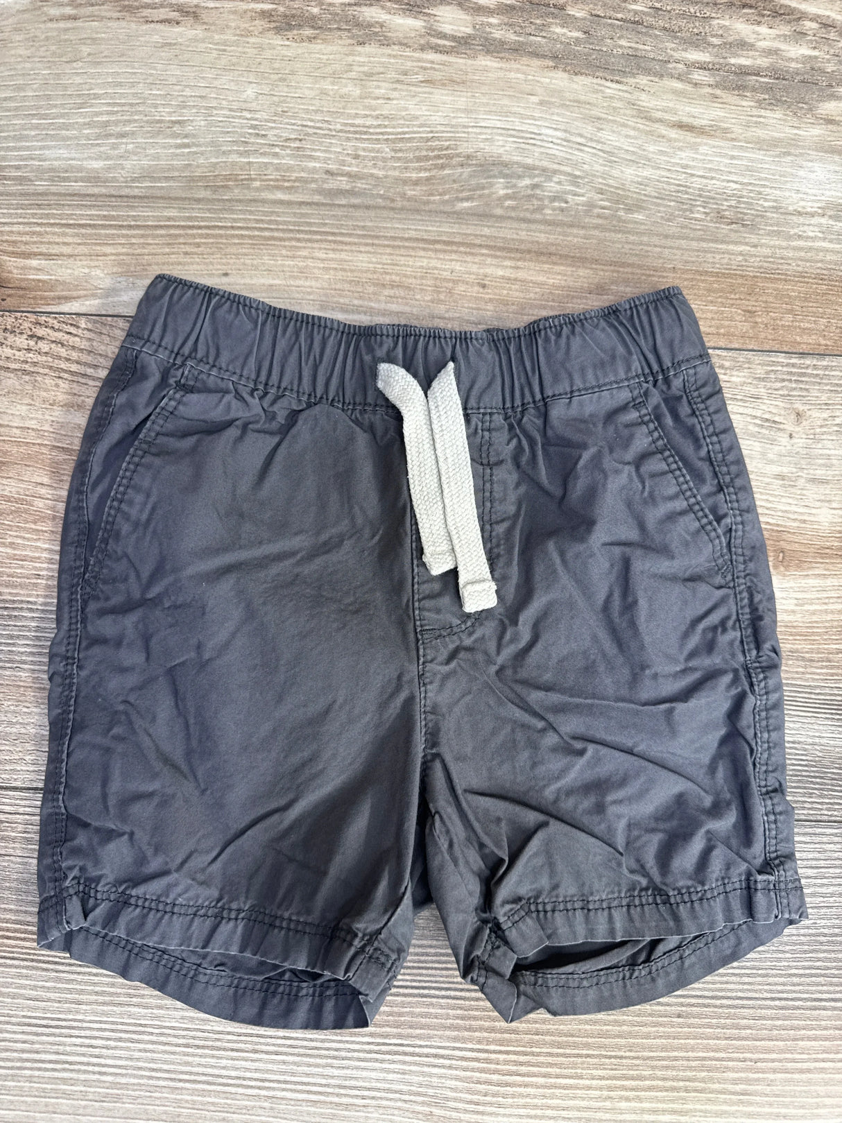 Flat lay of grey Old Navy toddler drawstring shorts showing elastic waistband with white drawstring and side pockets on light wood background