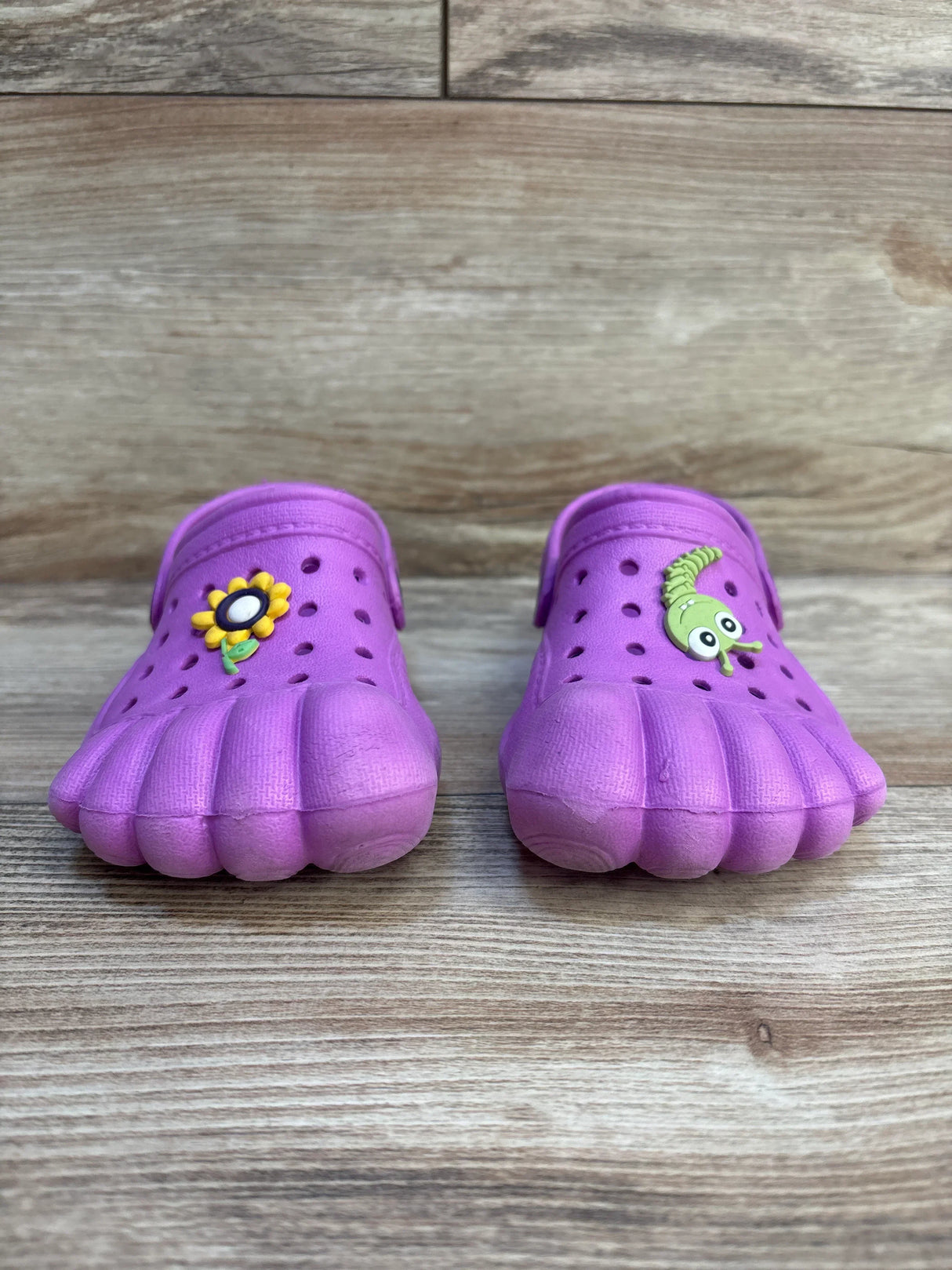 Purple kids toe shoes with sunflower and caterpillar charms on wooden floor