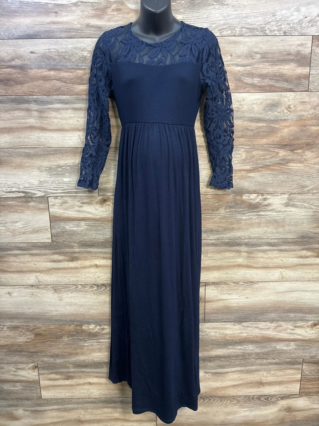 Front view of navy maternity maxi dress with lace long sleeves, sheer yoke and empire waist on wood plank background