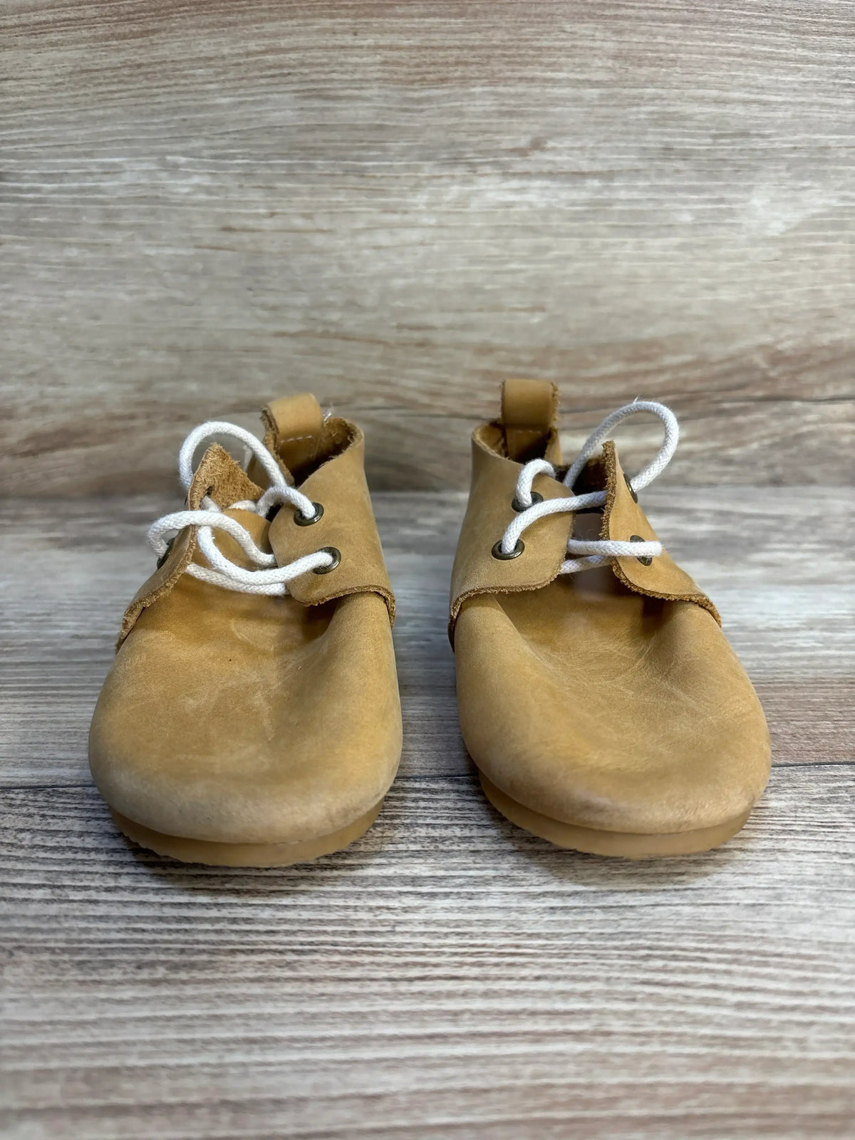 Front view of Piper Finn low-top oxford baby shoes showcasing tan leather upper and white laces on light wood background