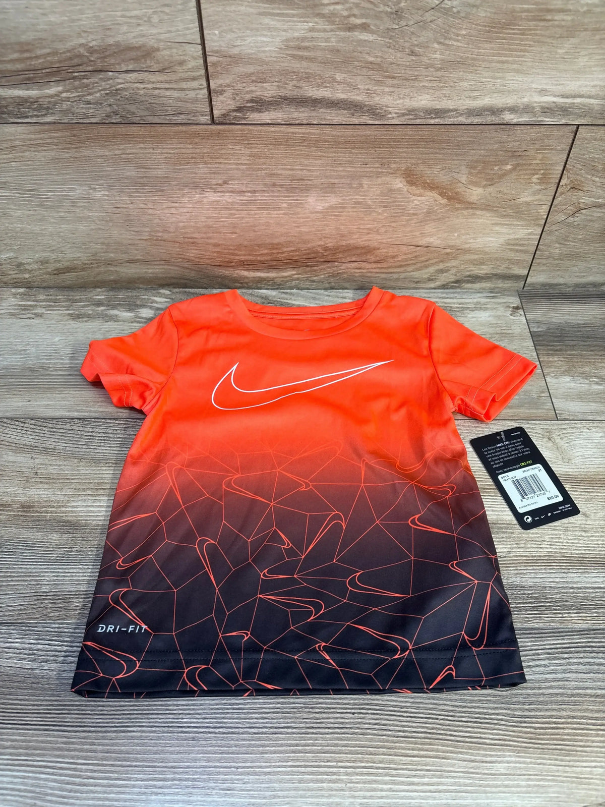 Flat lay of toddler orange Nike Dri-Fit shirt showcasing white swoosh and orange to black gradient with DRI-FIT text on wood floor