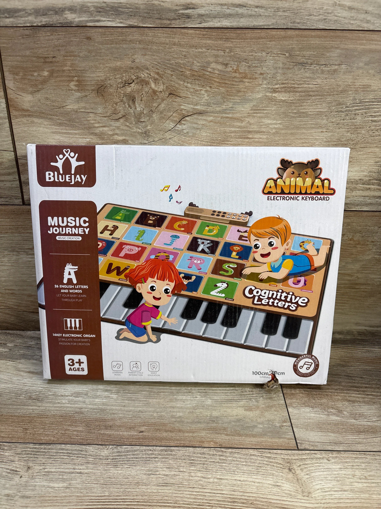 Front view of BlueJay animal electronic piano mat box showing keyboard with colorful alphabet tiles on wood floor