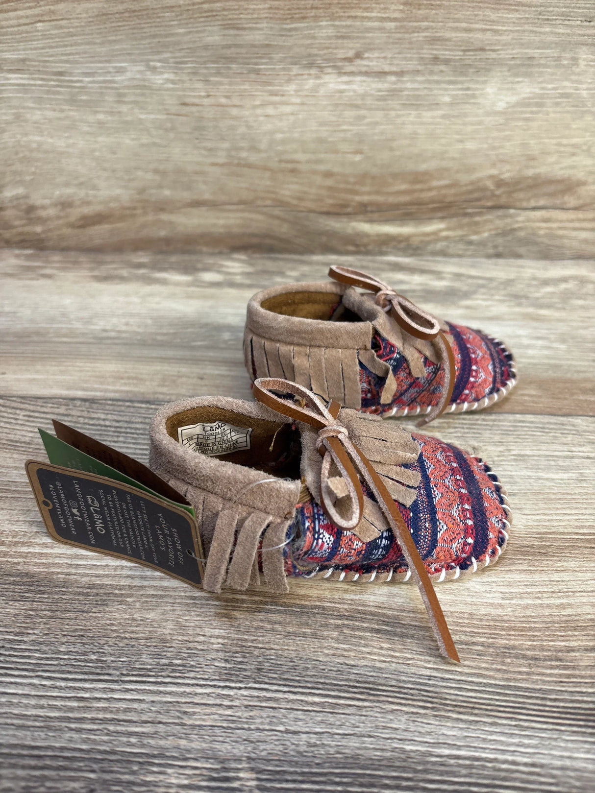Patterned suede baby moccasins with fringe and laces on wooden background