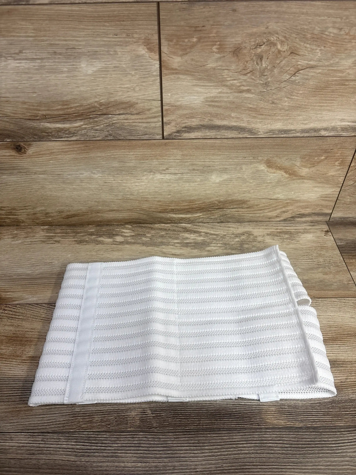 Top view of Gabriella abdominal and back support binder, white, folded, showing ribbed elastic and Velcro on wood