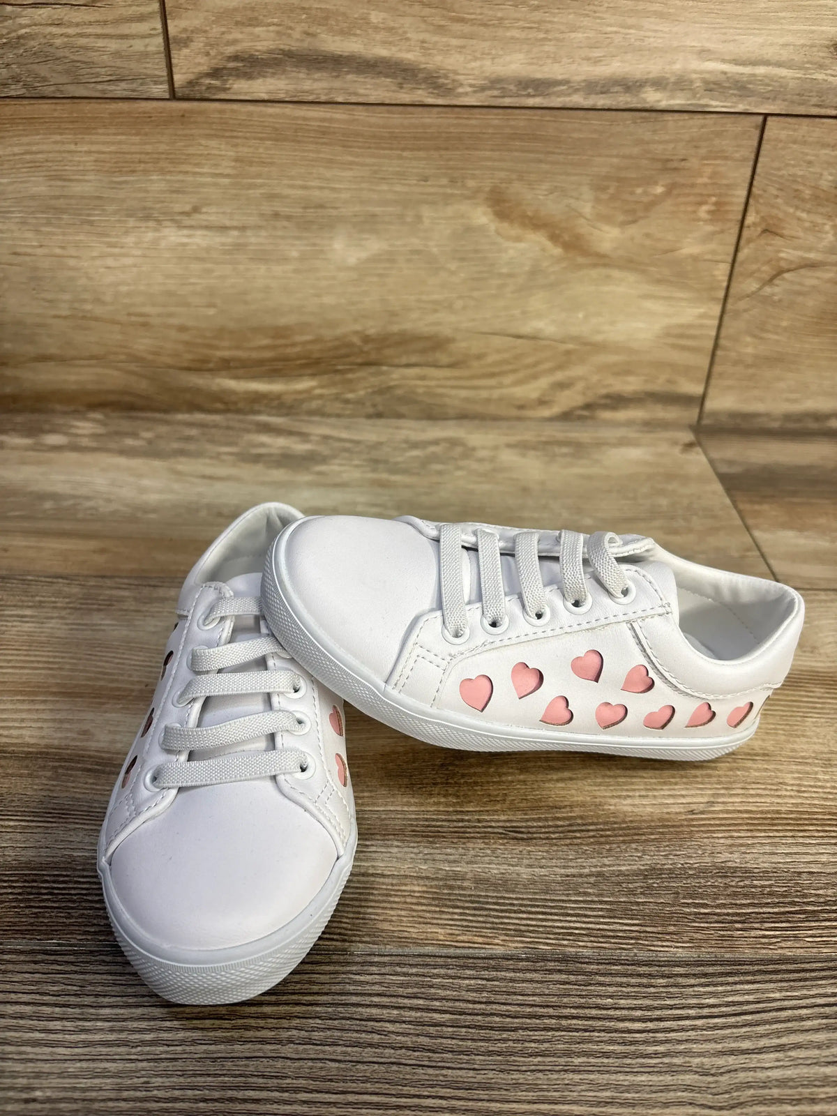 Front and side views of Janie & Jack heart sneakers showcasing white uppers, pink heart details, and bungee laces on a wood floor