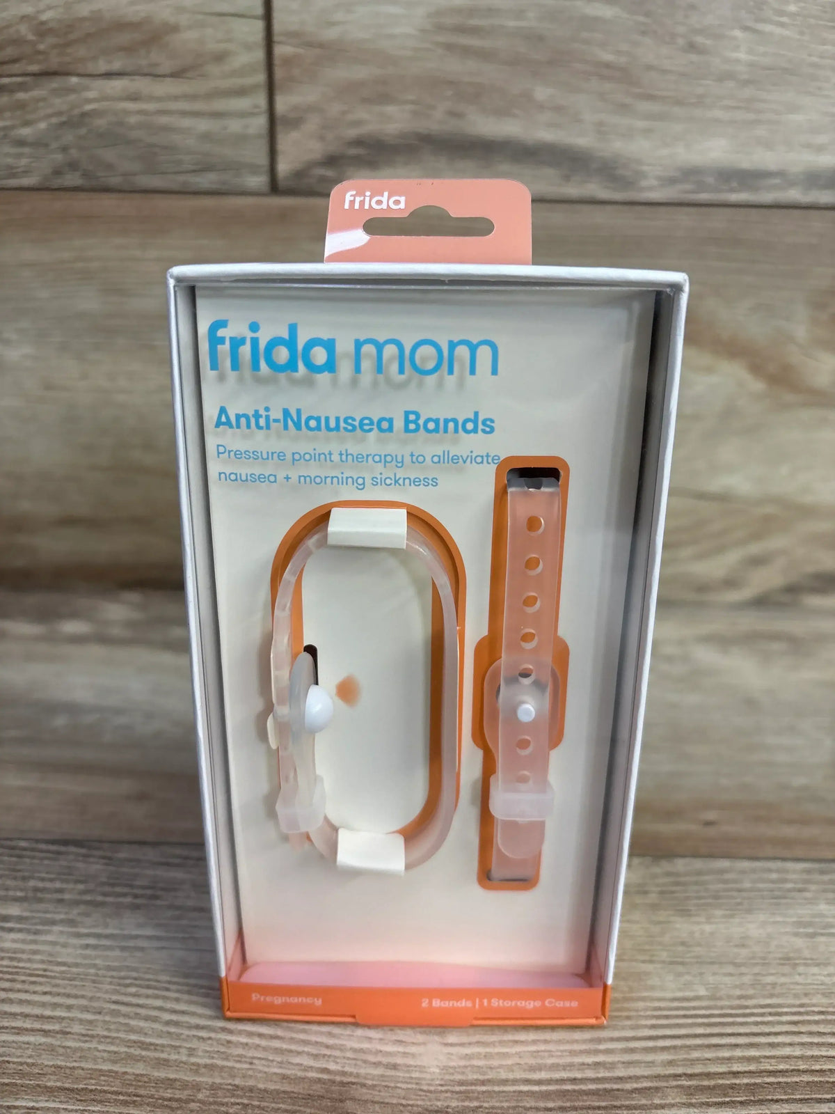 Front view of Frida Mom Anti-Nausea Bands showing two orange wristbands with white acupressure button on wood background