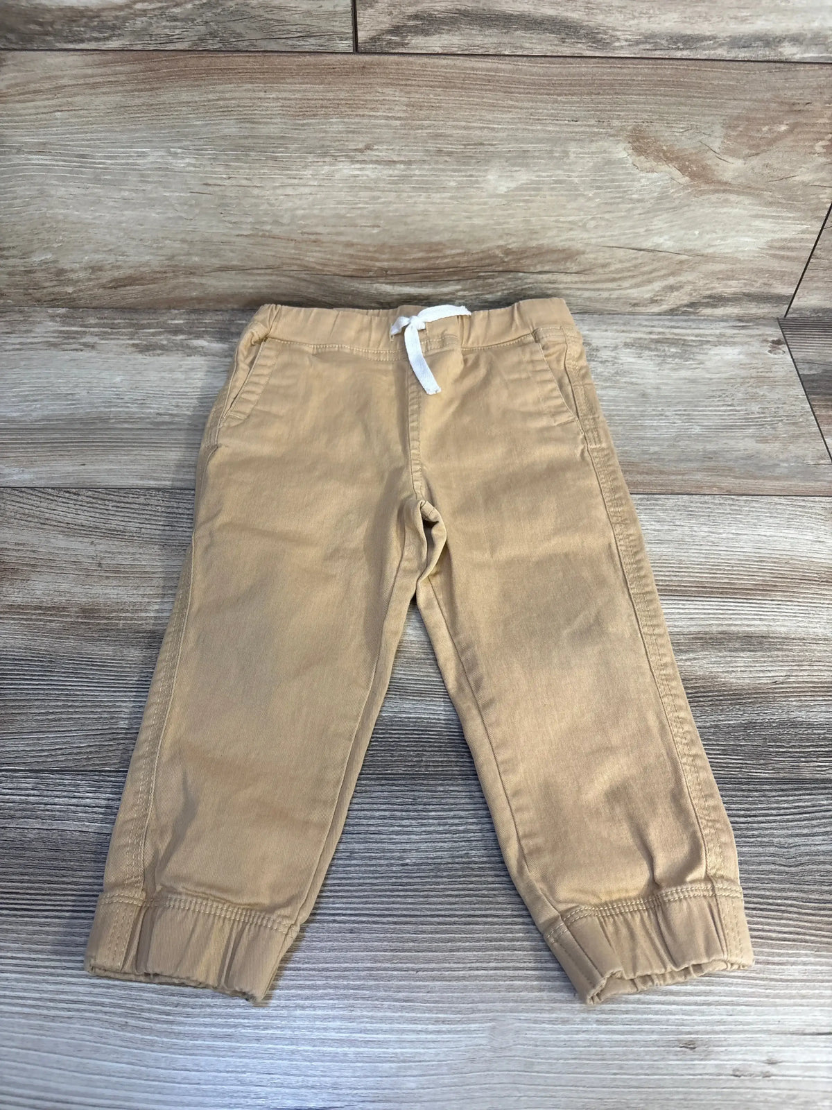 Beige toddler pants with elastic cuffs and white drawstring on wood background