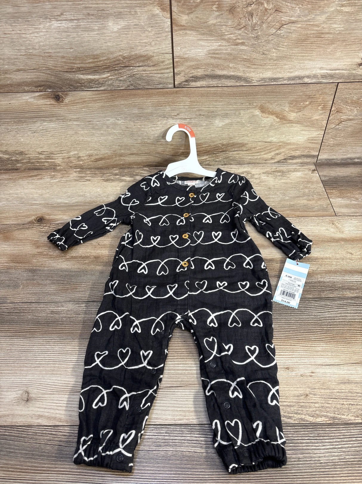 Black baby jumpsuit with white heart pattern on hanger, displayed on wooden floor, with tag