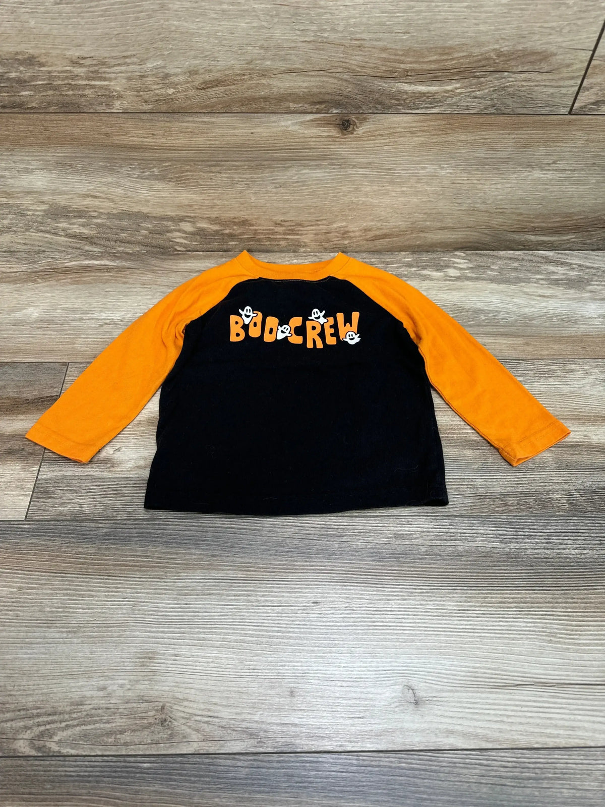 Front view of Jumping Beans Boo Crew shirt in orange and black with long sleeves and skull graphic on wood floor