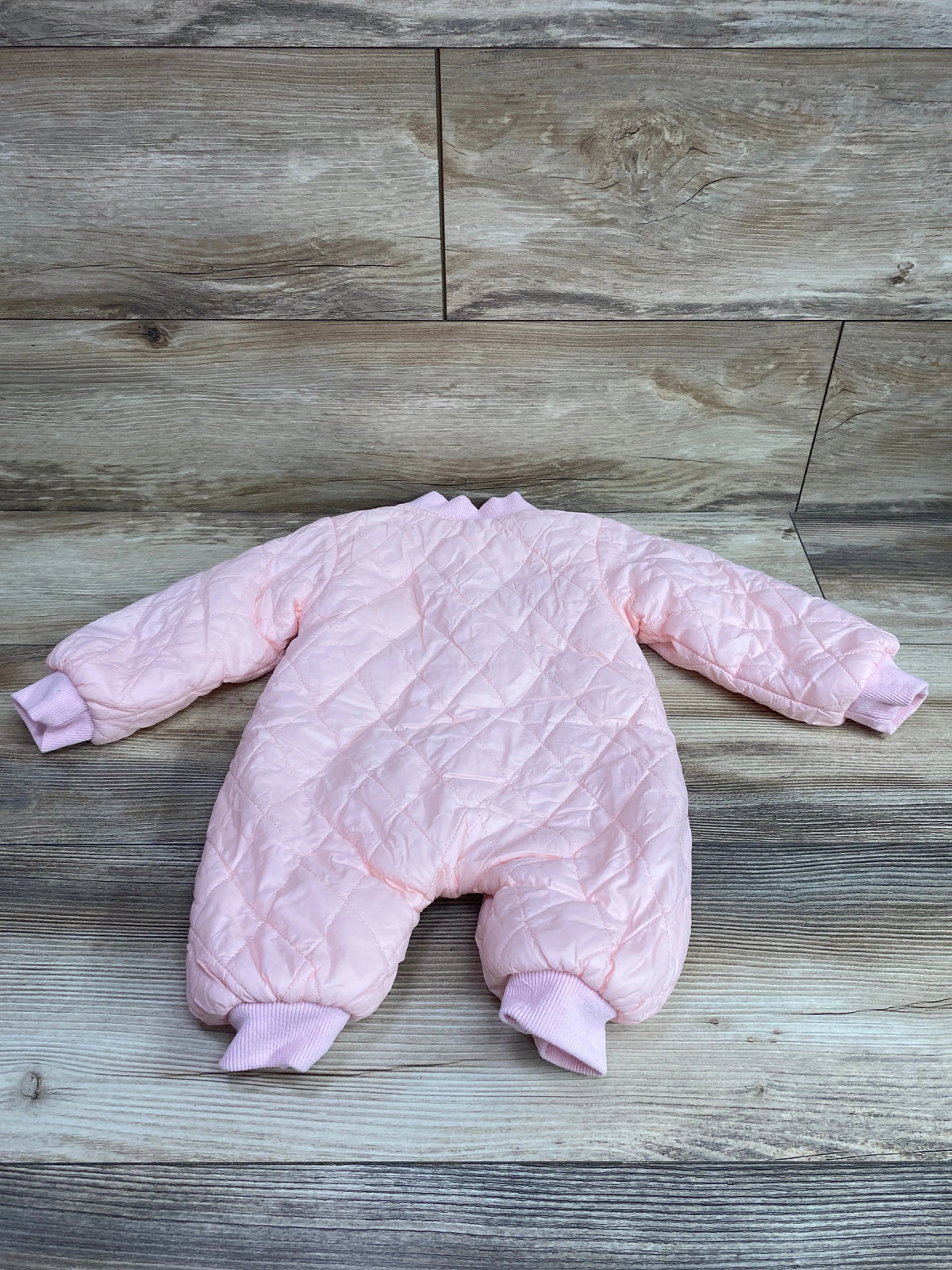 Flat lay of pink quilted coverall in size 3 months showcasing ribbed cuffs and ankle bands on wood-look flooring