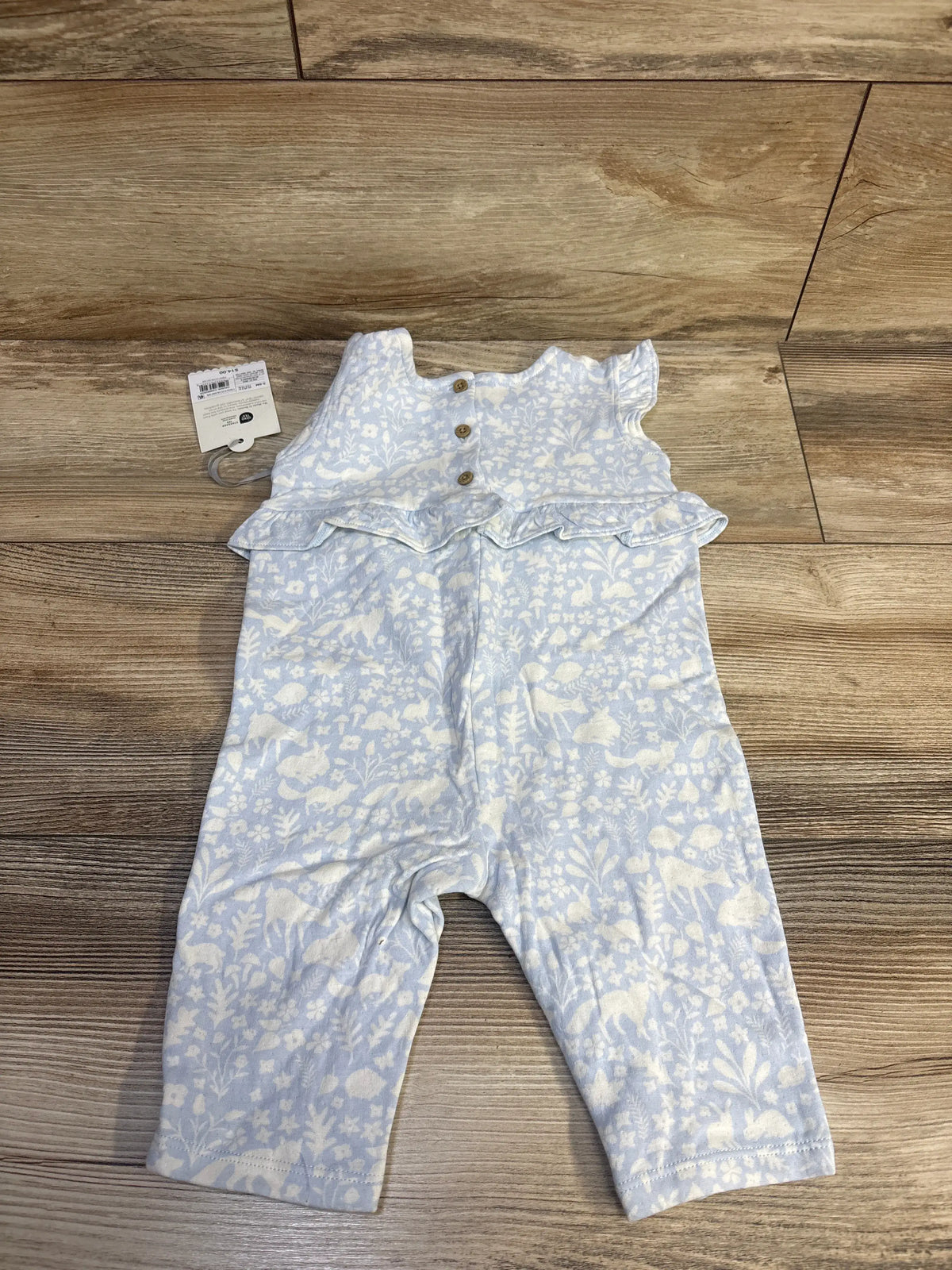 Top-down view of blue Cloud Island baby jumpsuit with white floral and animal print, ruffled waist, and flutter sleeves