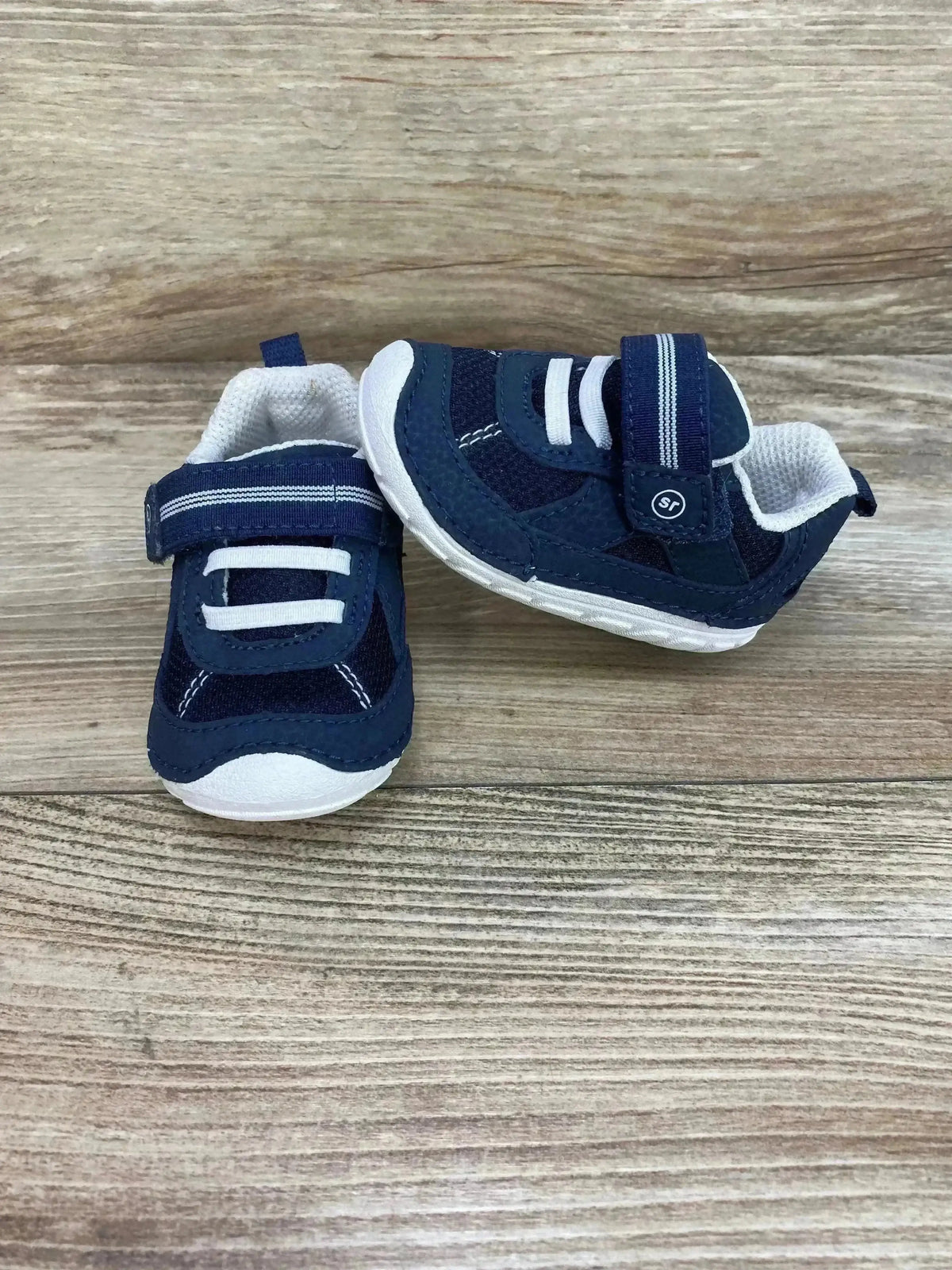 Front and side view of Stride Rite Jamie navy and white baby sneaker showing velcro strap and white sole on wood background