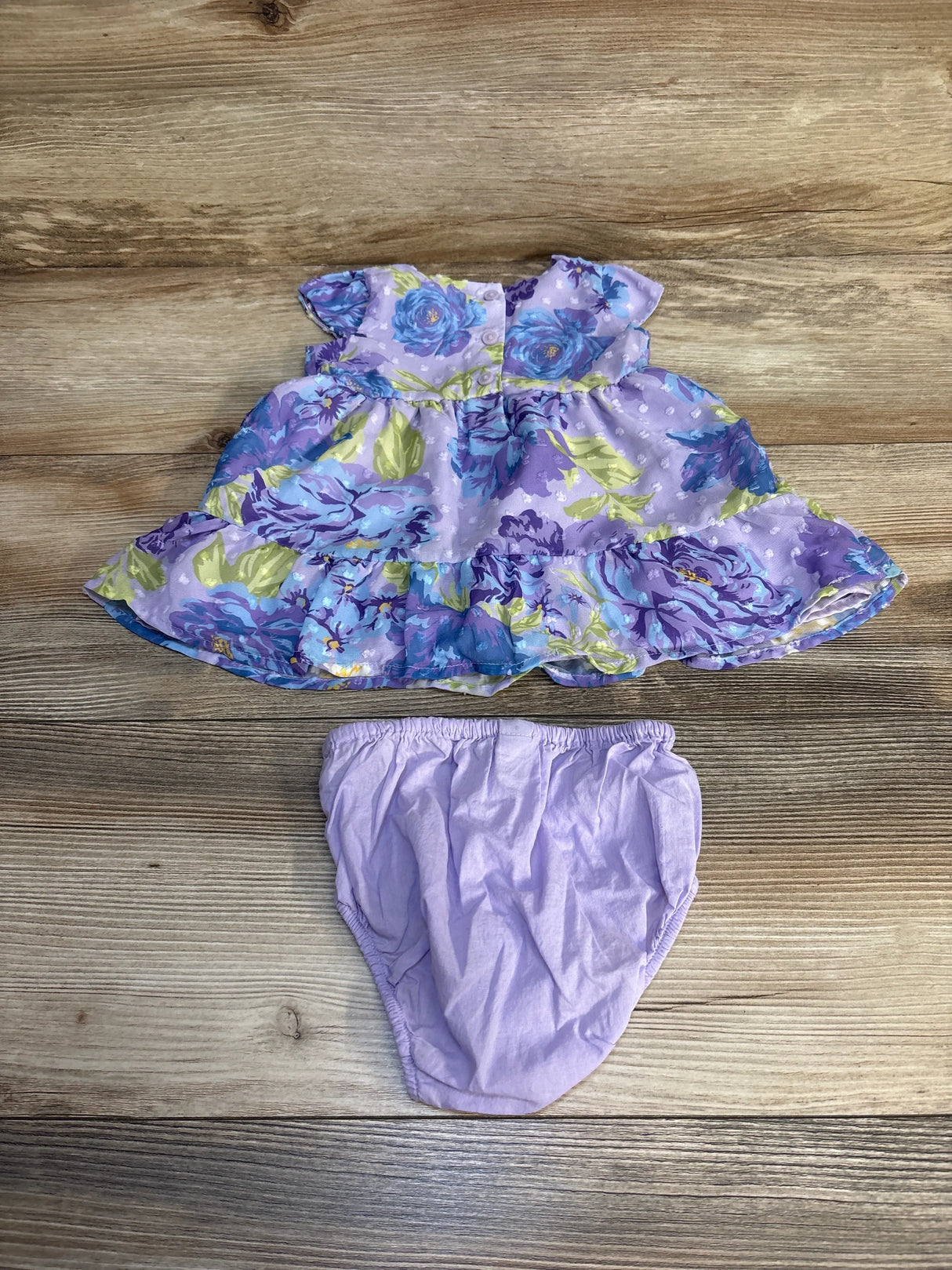 Purple floral baby dress with matching diaper cover on wood background