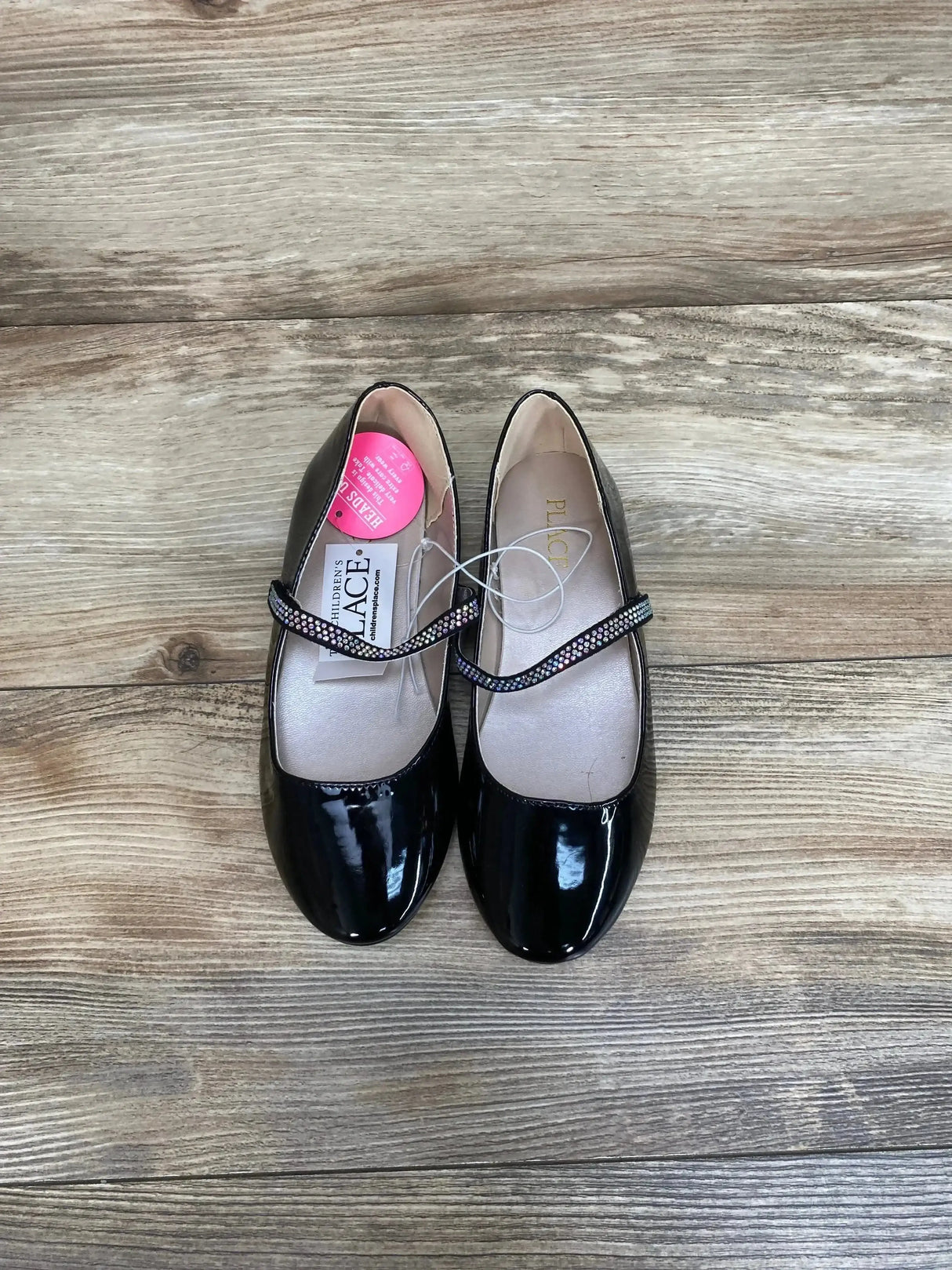 Side view of pair of black girls’ faux patent leather ballet flats showing jeweled bow detail on white background