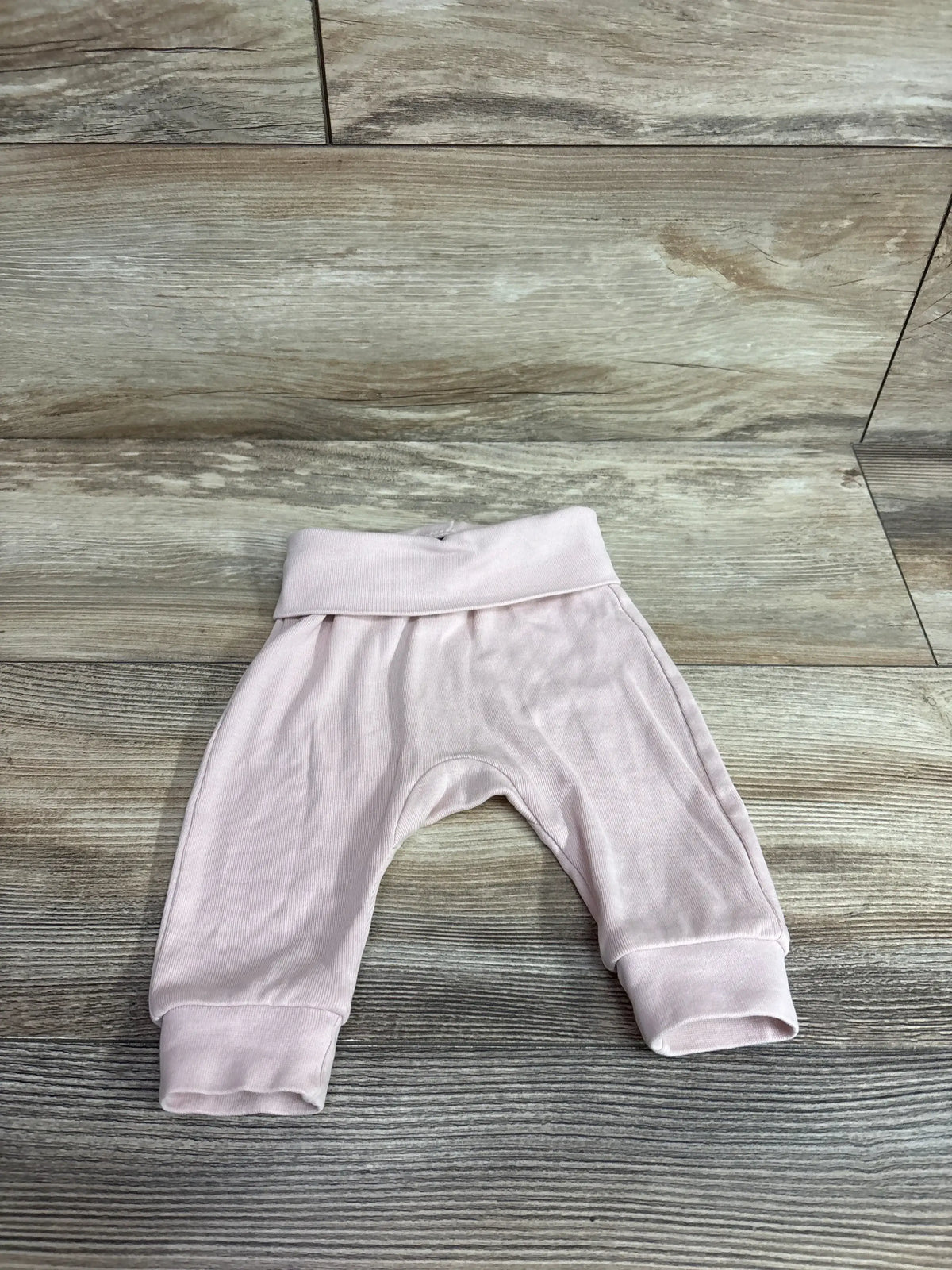 Flat lay of pink H&M foldover-waist baby pants showing fold-over waistband and cuffed legs on wood background