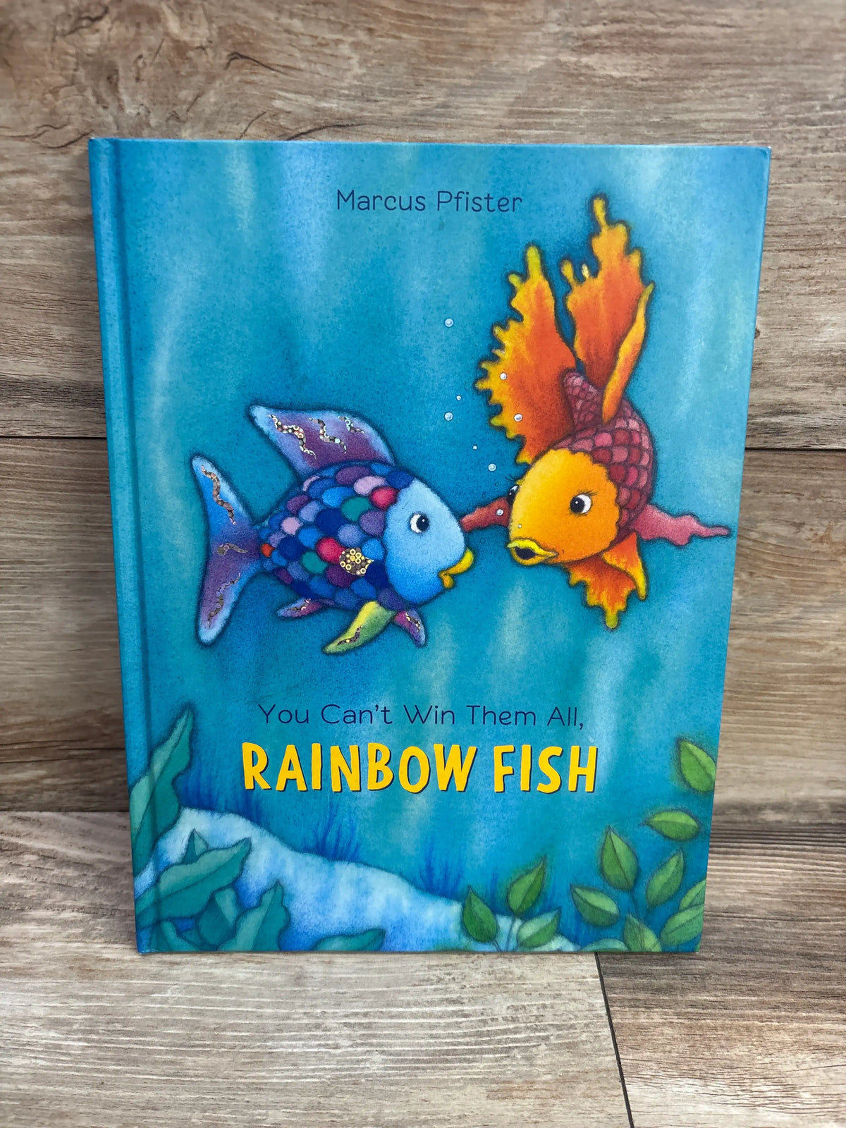 Front cover of The Rainbow Fish hardcover book showing two colorful fish and underwater plants with a wood-grain background