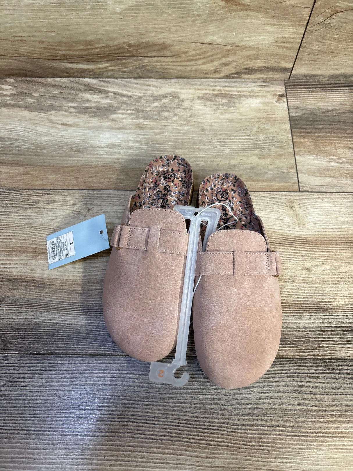 Top view of Cat & Jack Perry toddler clogs, blush suede-like upper and floral insole, size tag and hanger on wood floor