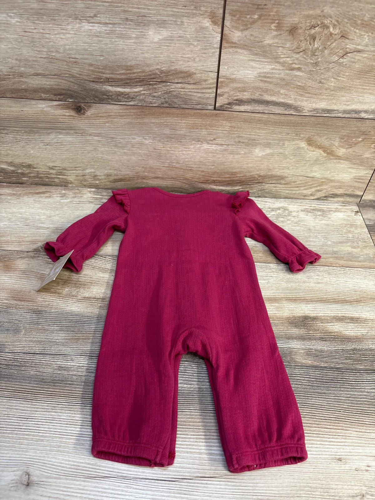 Back view of Little Me organic coverall in hot pink showcasing ruffle shoulder and cuff details on wood floor background