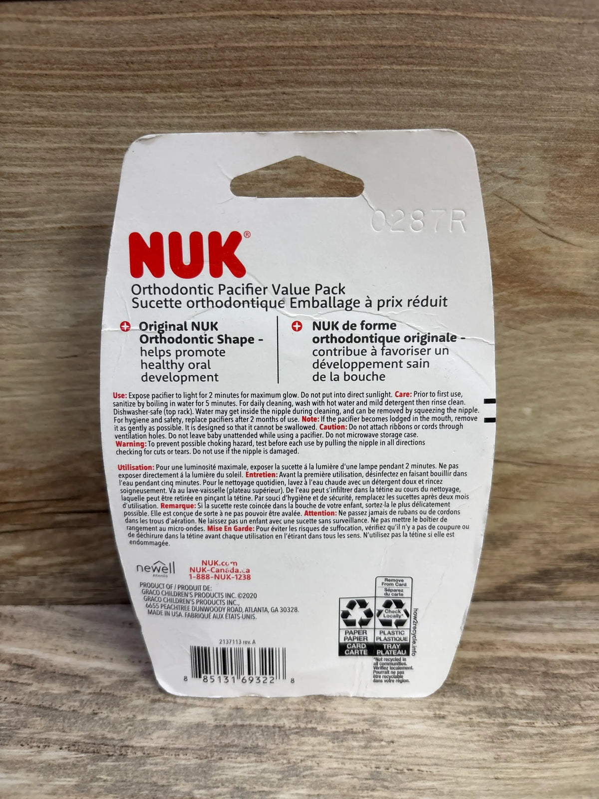 Back view of NUK 3pk orthodontic pacifiers, pink 0-6m, showing value-pack packaging on a wood-grain background