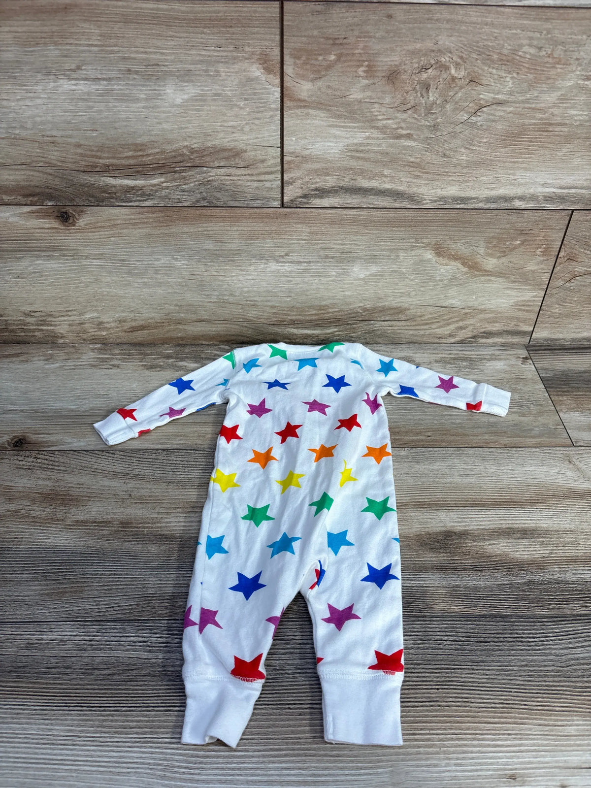 Front view of Primary organic star print sleeper showcasing multicolored stars and long sleeves on a wood-grain background