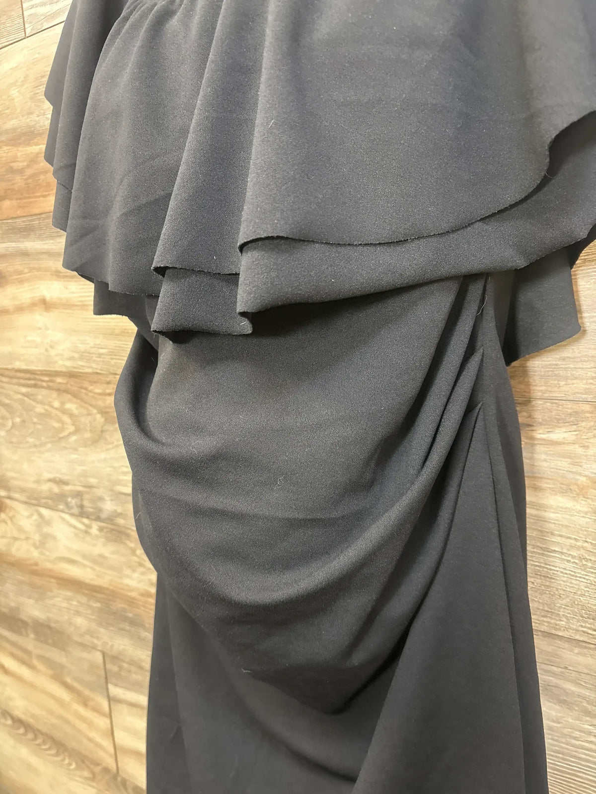Close-up of My Bump Ruffle Off The Shoulder Dress Black sz XL showcasing layered ruffles and draped fabric on a wood floor
