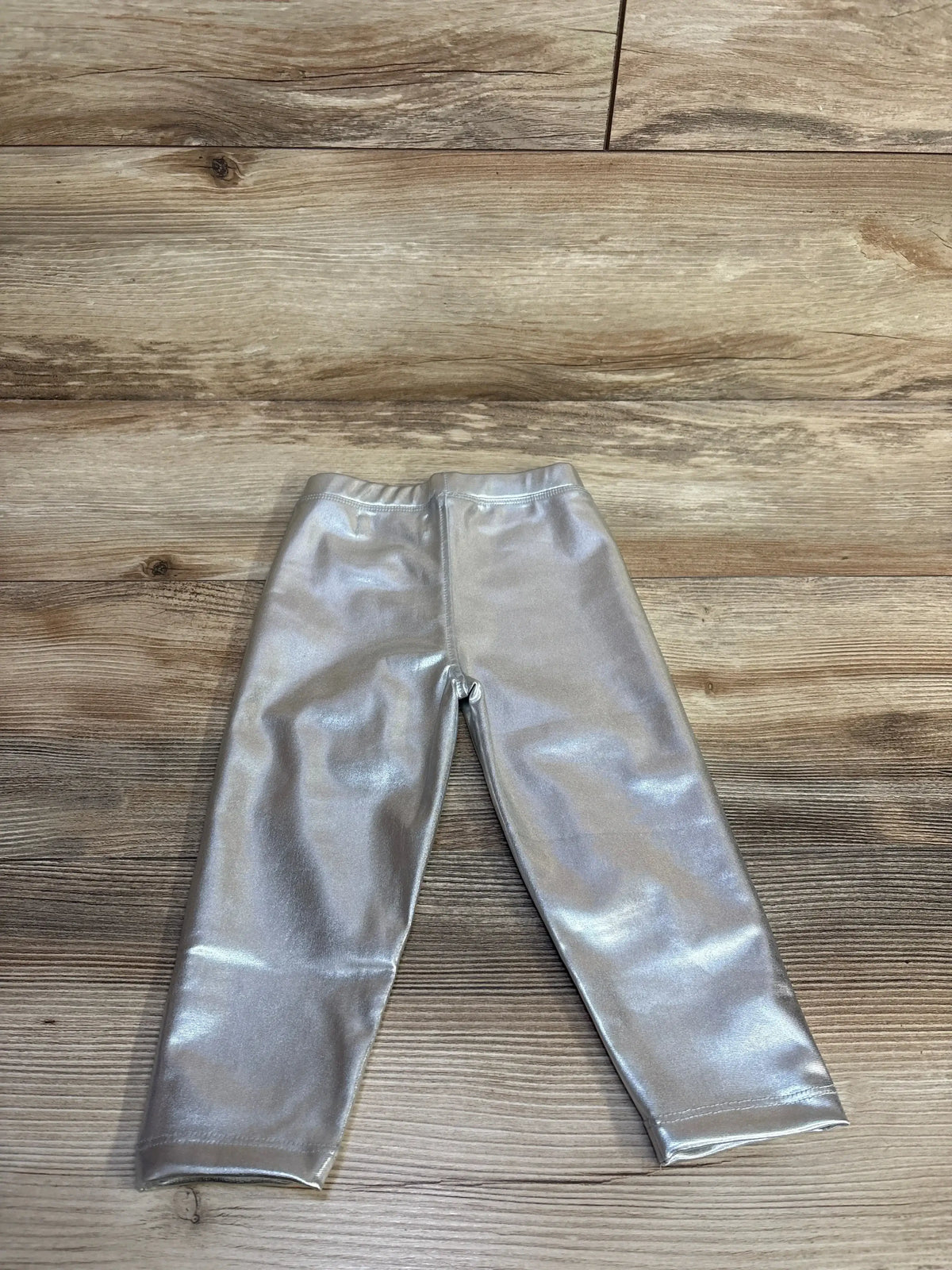 Flat lay of toddler metallic silver leggings showing shiny stretch fabric and elastic waistband on wood floor background
