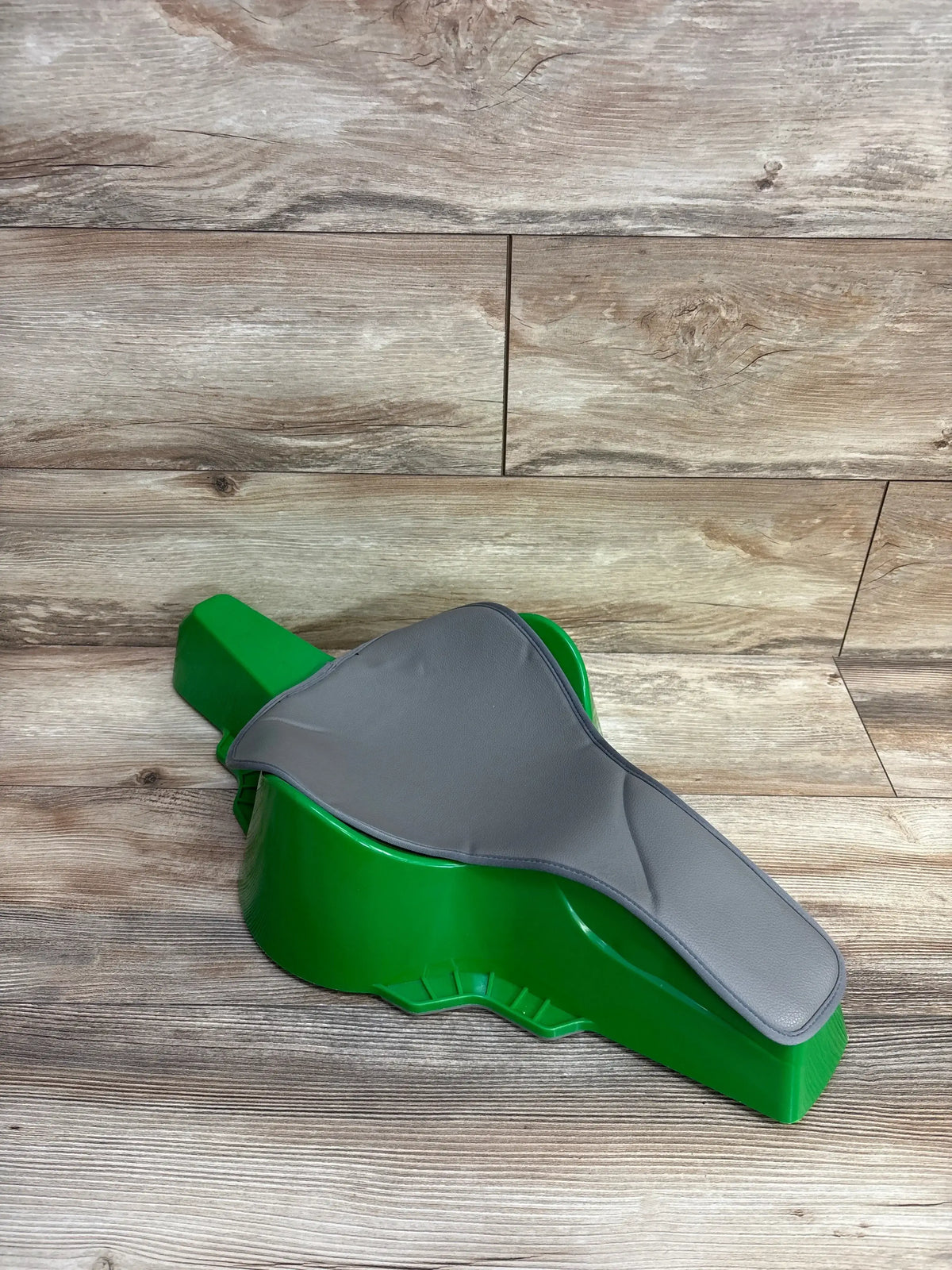 Angled top view of Crawligator Tummy Time Toy in green showing removable gray padded seat on wood floor background