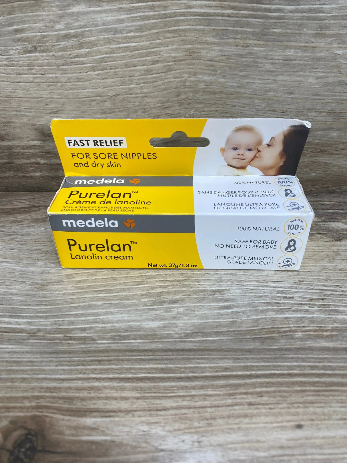 Front view of Medela Purelan lanolin nipple cream 1.3oz yellow box showcasing baby photo and 100 percent natural label on wood plank floor