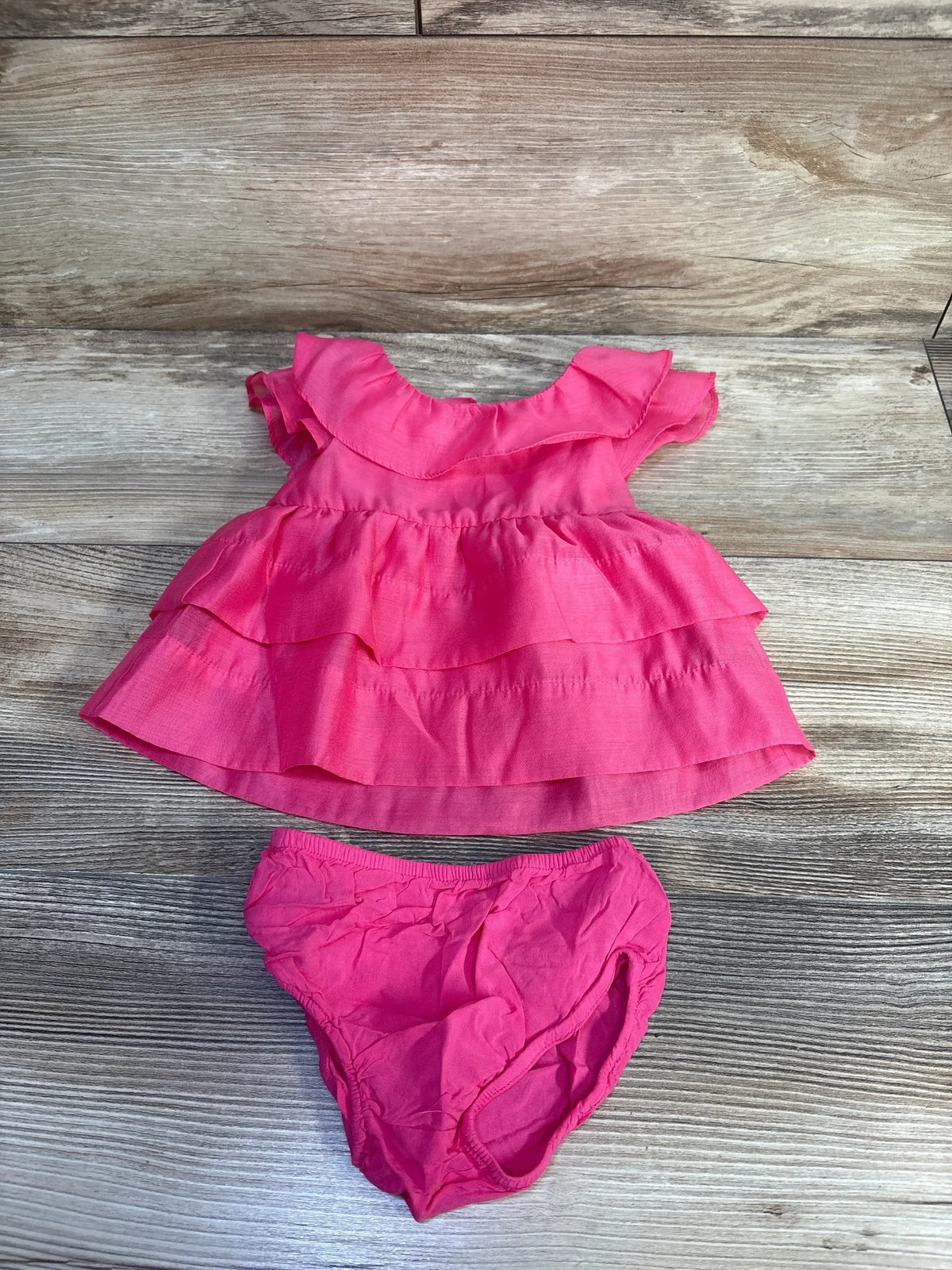 Flat lay of newborn pink Cat & Jack 2-piece flutter sleeve dress with tiered ruffle skirt and matching diaper cover on wood background